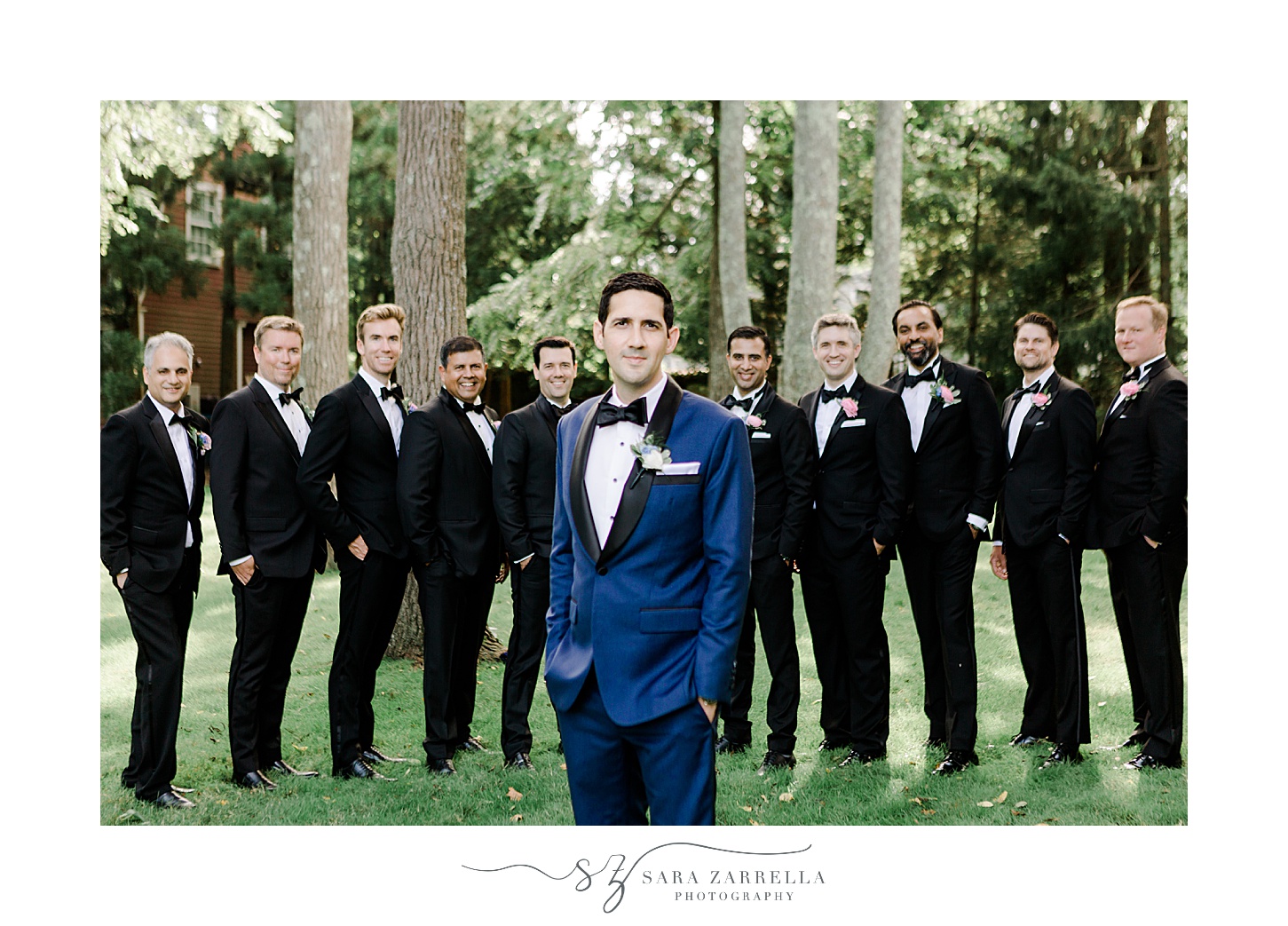 groom in blue suit jacket poses with hands in pockets in front of groomsmen in black suits 