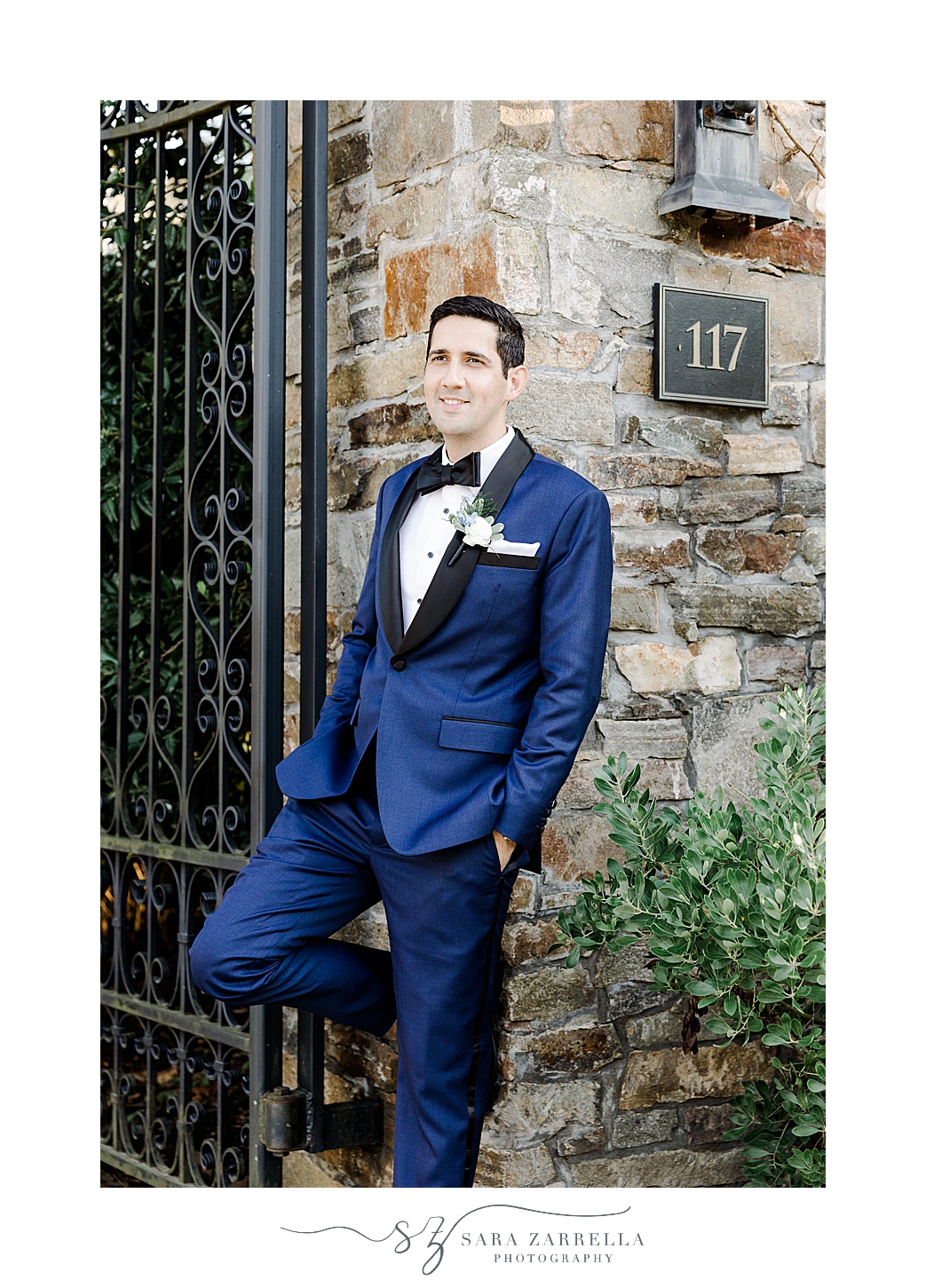 groom in blue suit jacket leans against stone gate at the Chanler