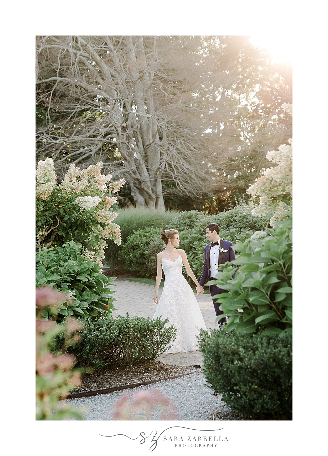 newlyweds hold hands walking between bushes at the Chanler 