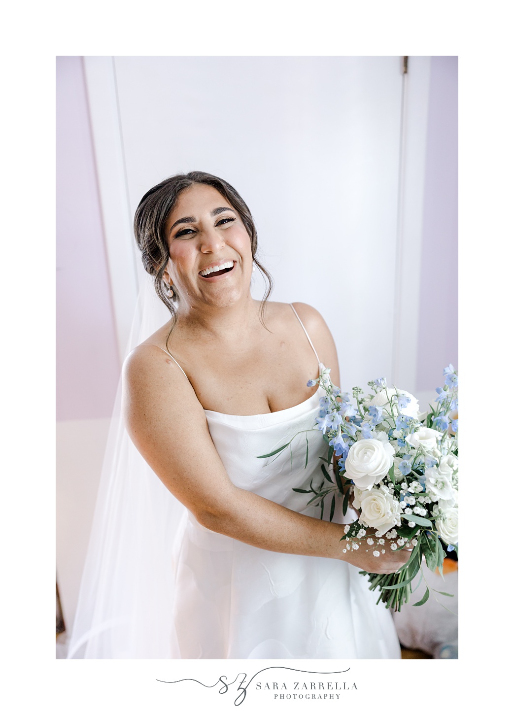 bride laughs holding blue and white bouquet on hip in Rhode Island home