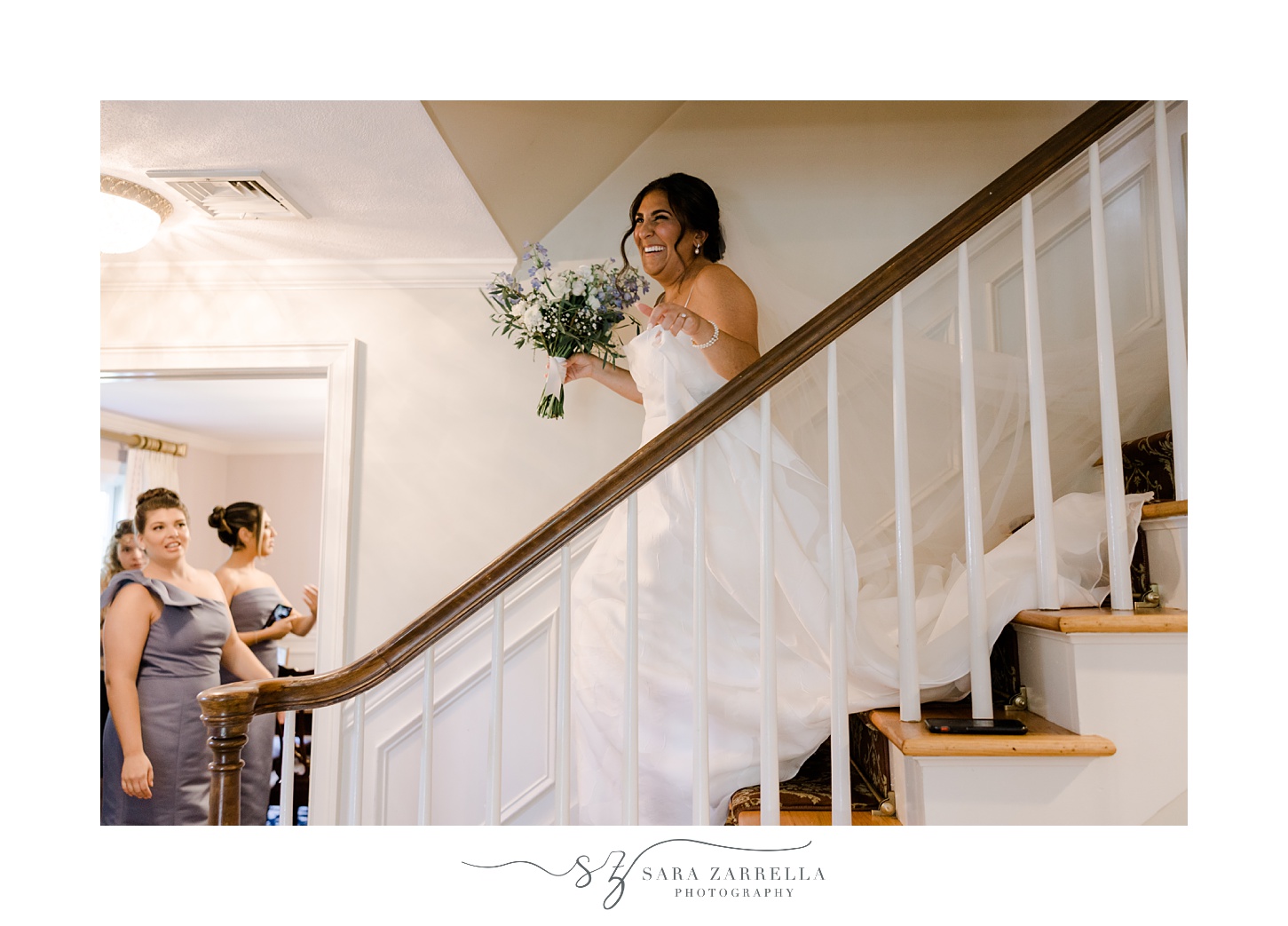 bride walks down steps inside home carrying blue and white floral bouquet in Rhode Island 