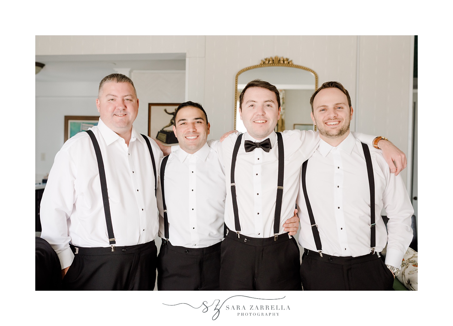 groom hugs groomsmen around shoulders with black suspenders and black bow ties 