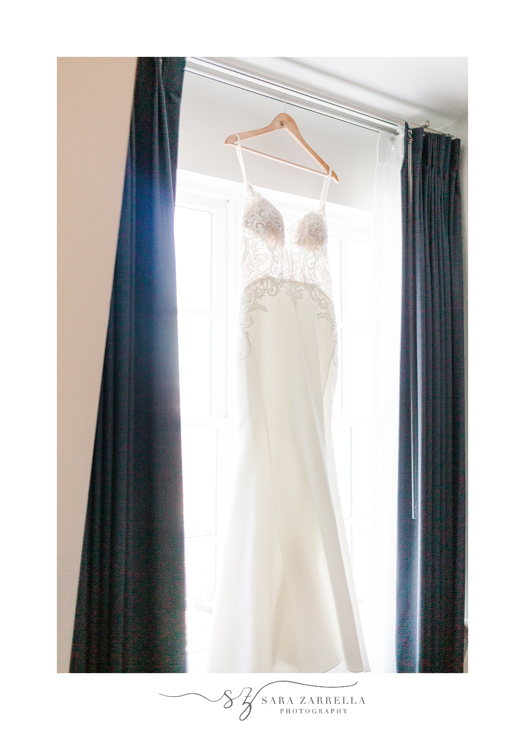 wedding gown hangs in window between navy curtains at Regatta Place