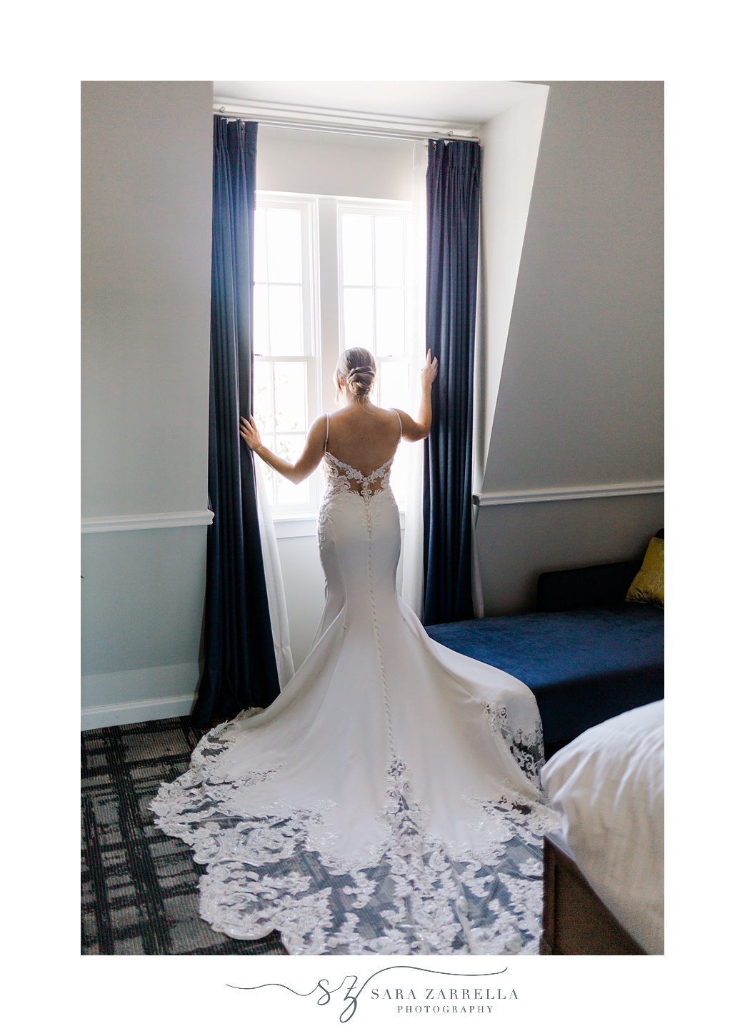 bride stands in window looking over Newport RI in wedding gown with lace edging 