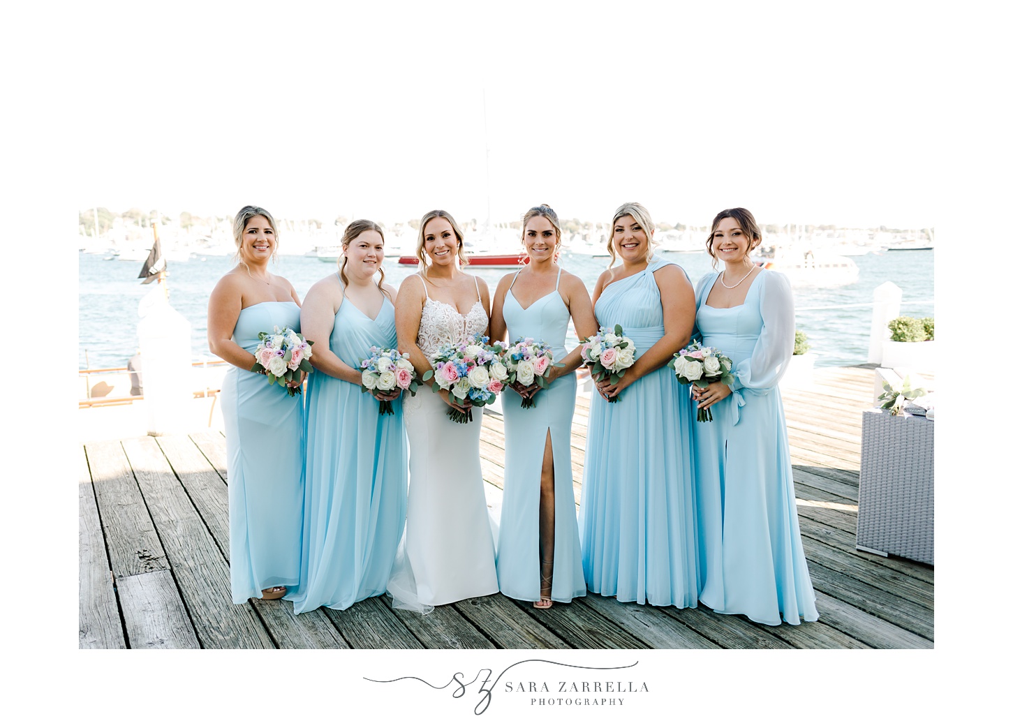 bride stands with bridesmaids in light blue gowns on dock at Regatta Place