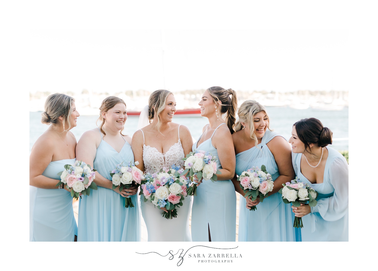 bride laughs with bridesmaids in blue gowns on dock at Regatta Place