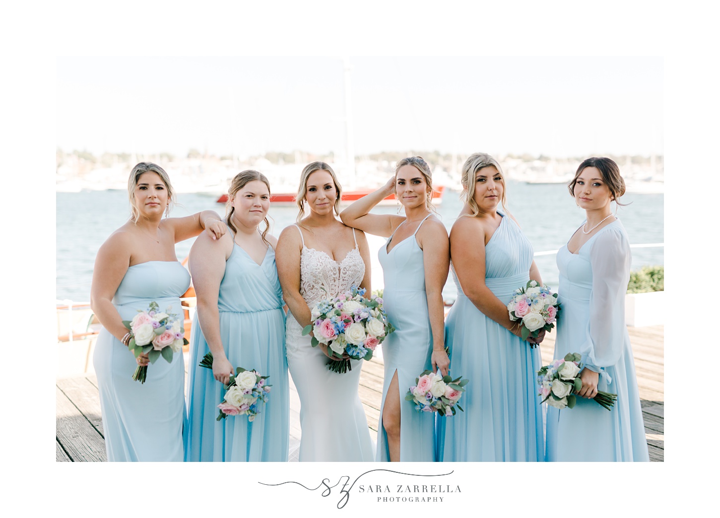 bride and bridesmaids in blue gowns stand on dock at Regatta Place