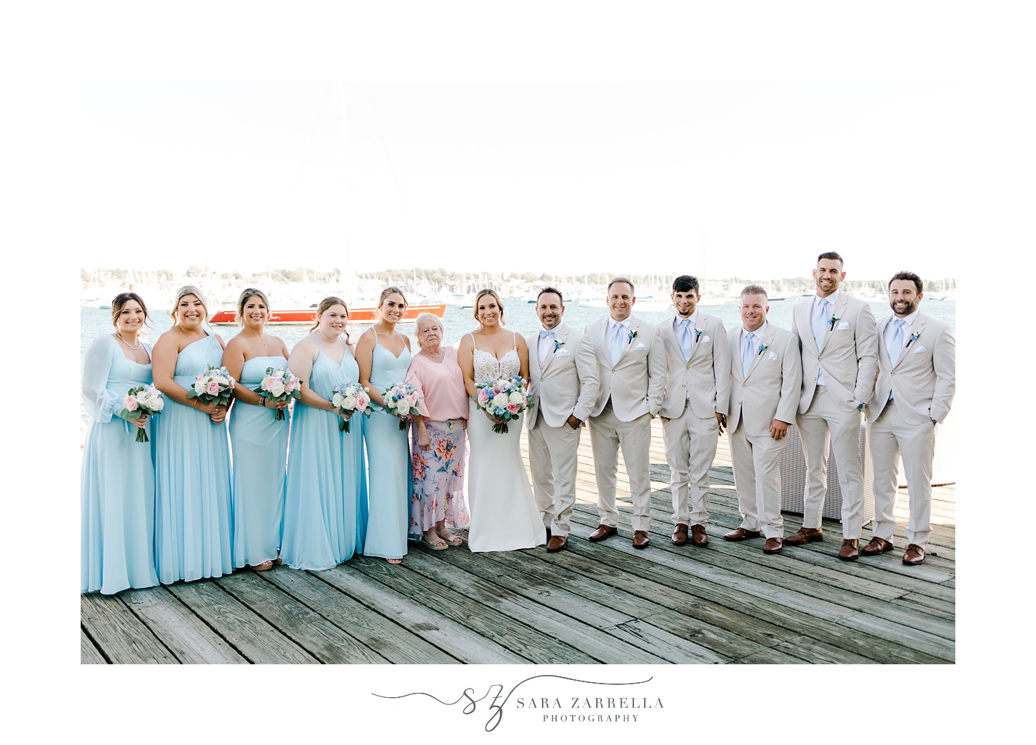 bride and groom stand with wedding party in blue and tan attire on dock at Regatta Place