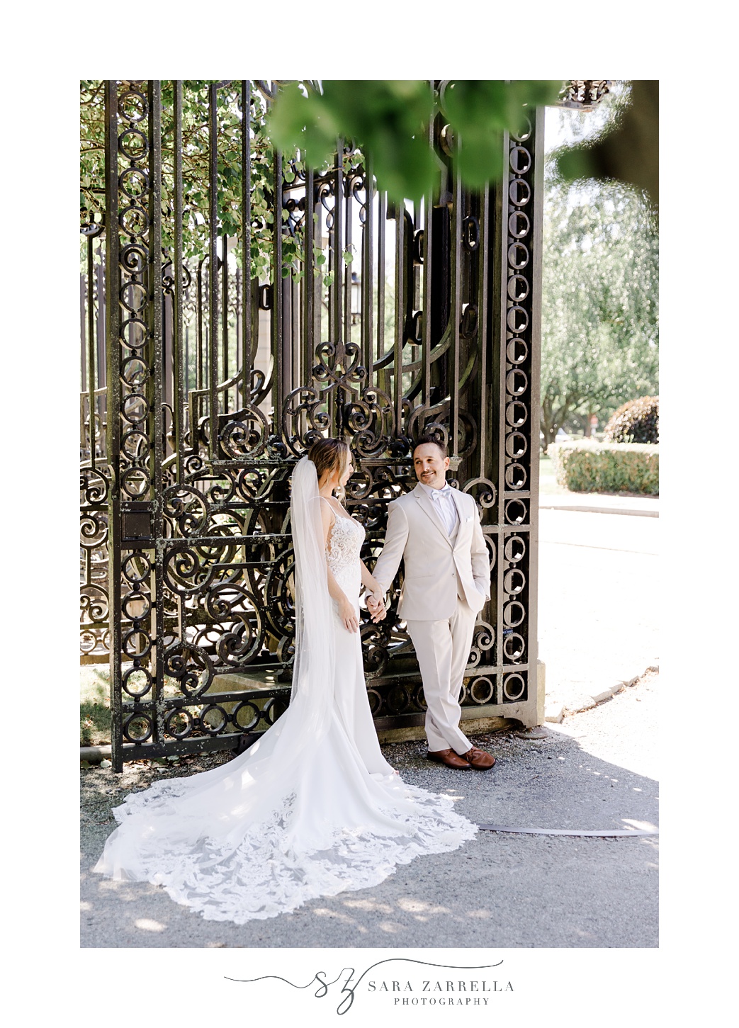 bride and groom hold hands leaning against gate of Newport mansion
