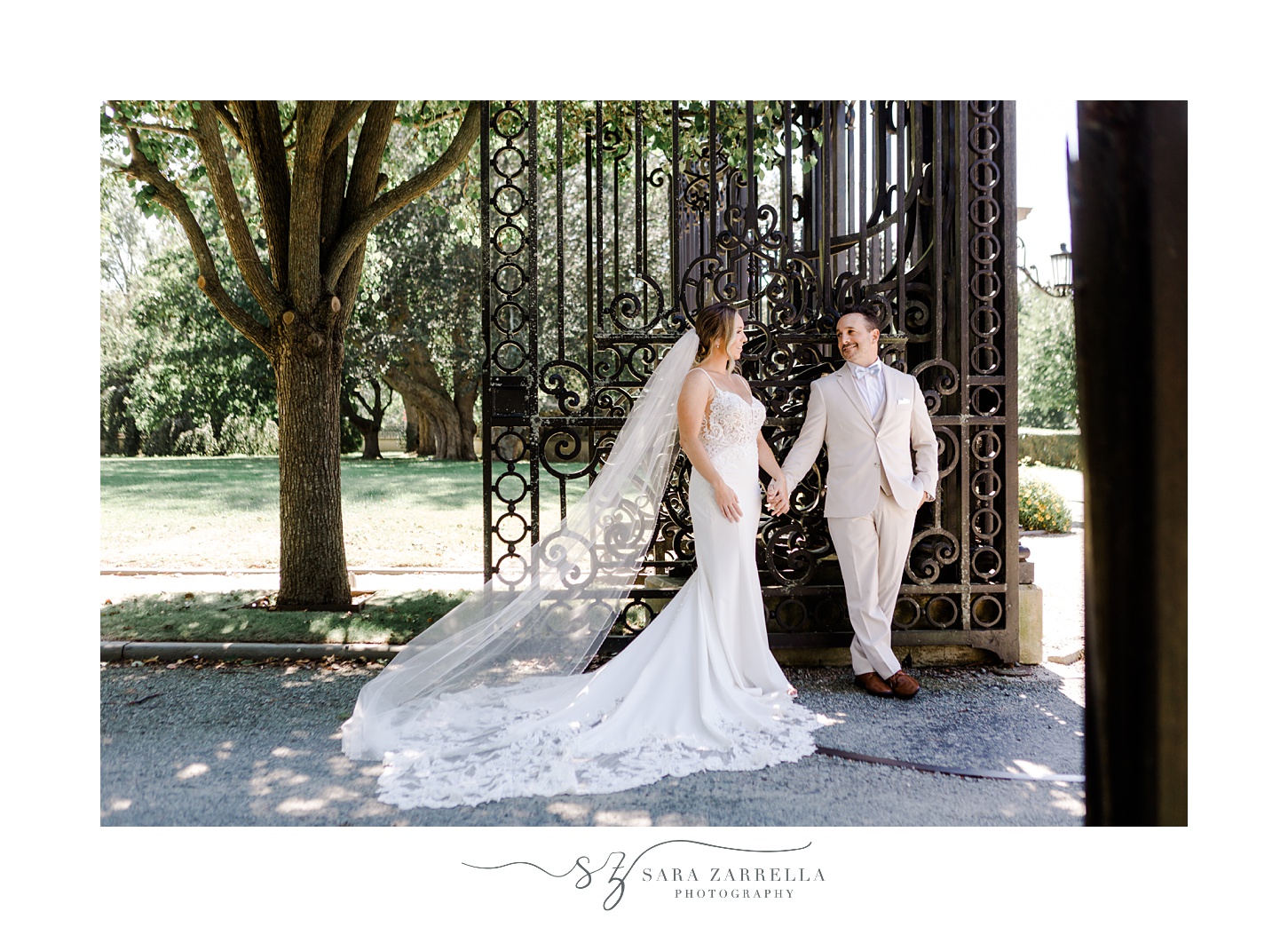 newlyweds stand holding hands leaning against gate of Newport mansion