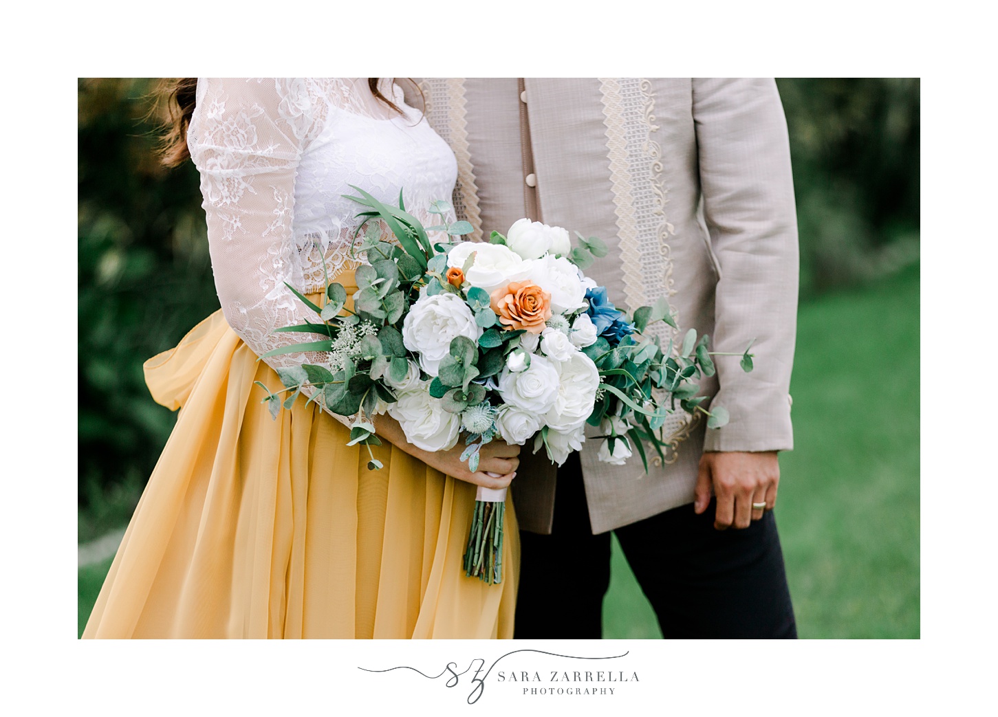 bride holds bouquet of white, blue, and orange silk flowers hugging groom