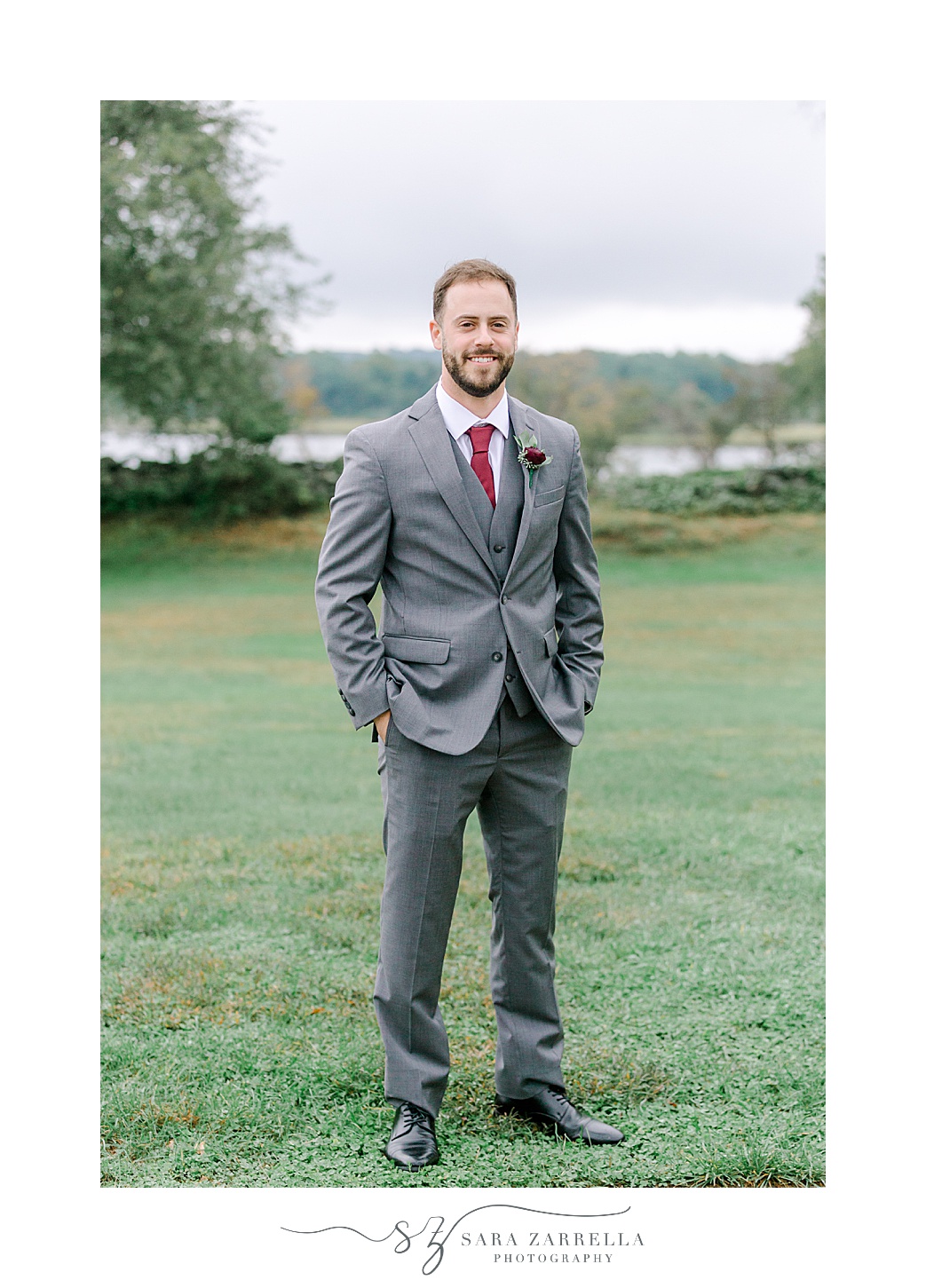 groom poses in grey suit with red tie and boutineere 