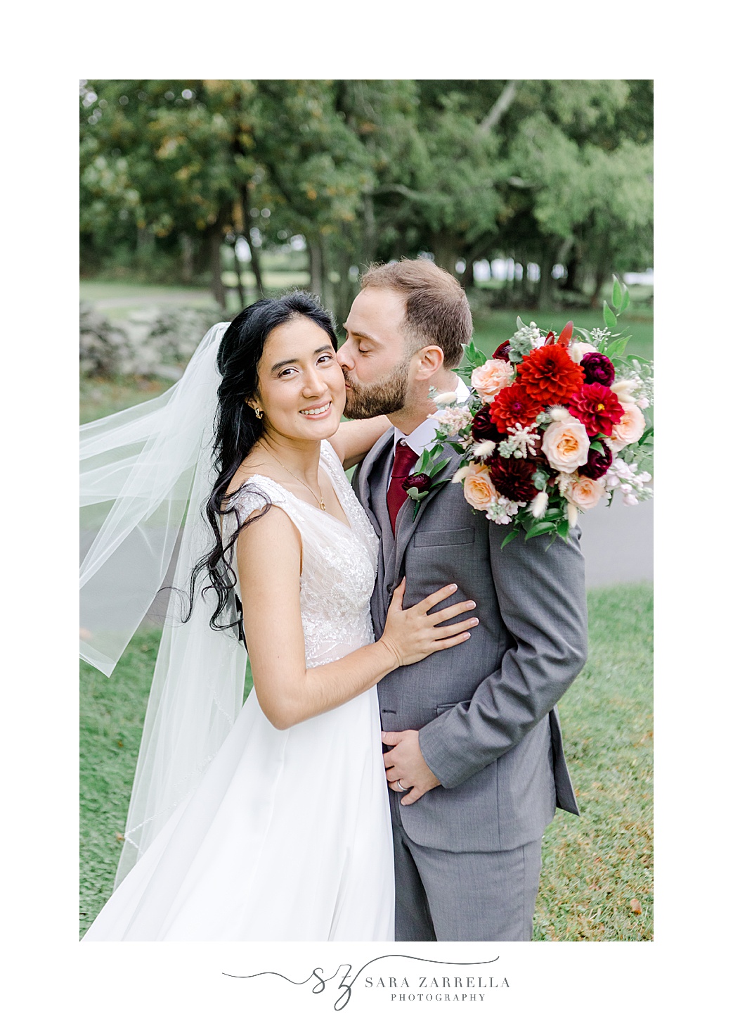 groom kisses bride's cheek with veil floating behind her