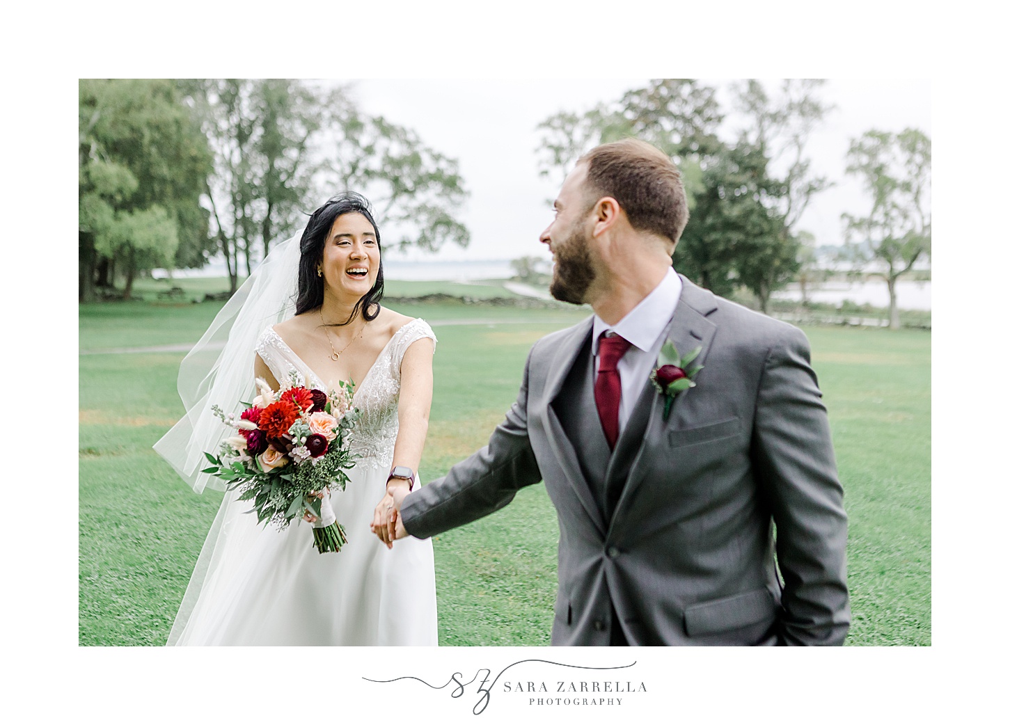groom in grey suit leads bride across lawn at Colt State Park