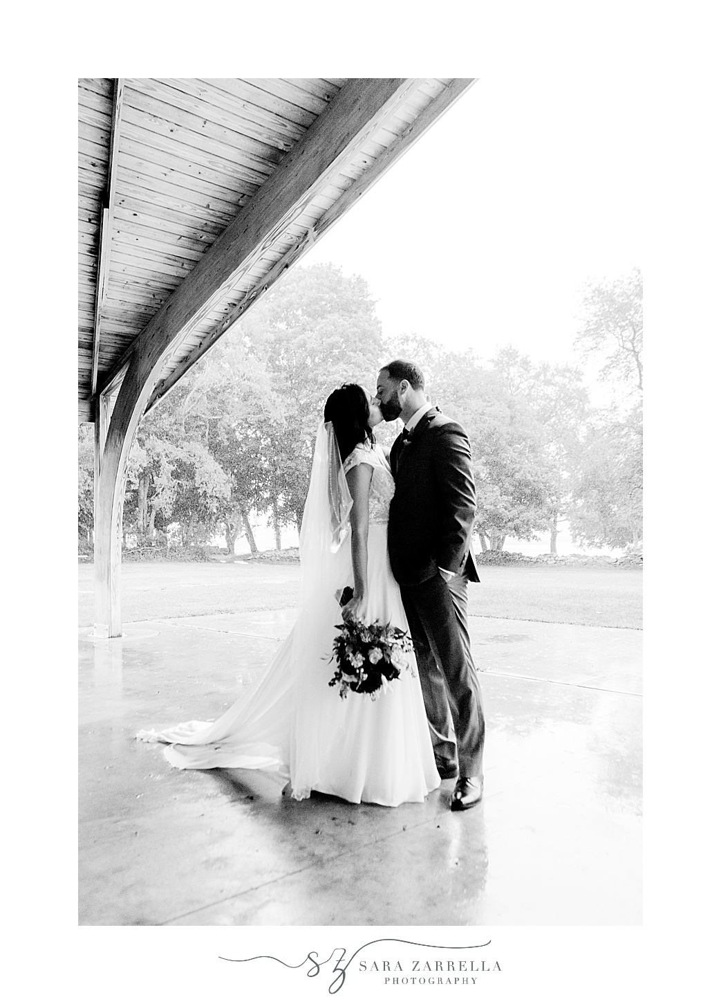 bride and groom kiss under shelter inside Colt State Park on rainy wedding day