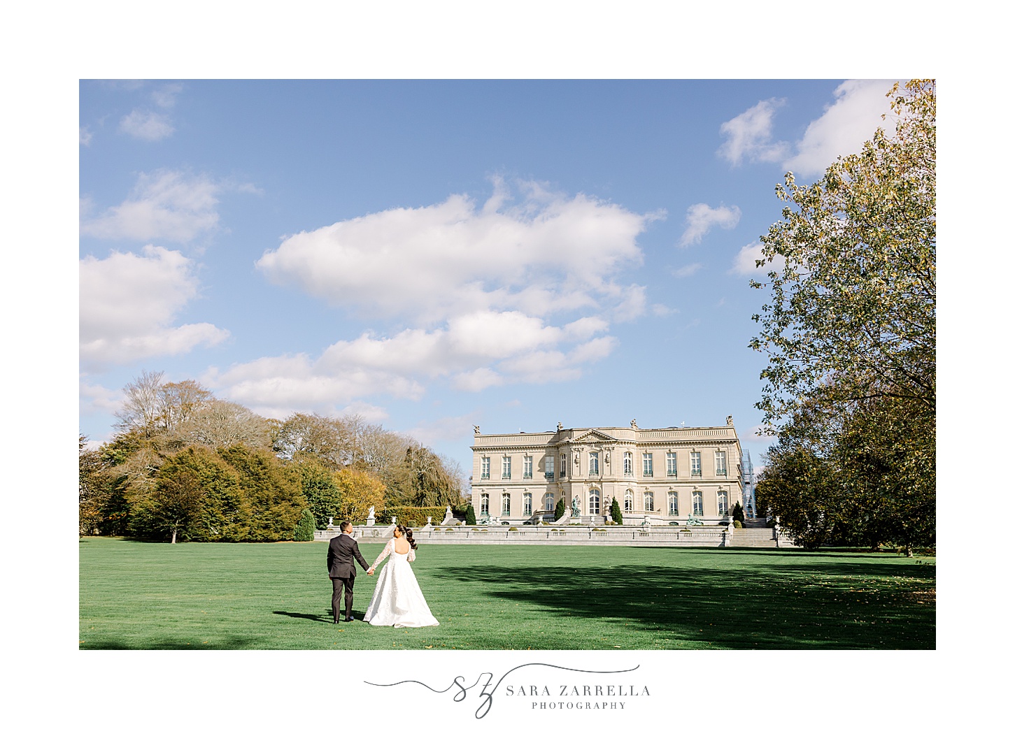 bride and groom walk across green lawn in front of mansion at the Elms