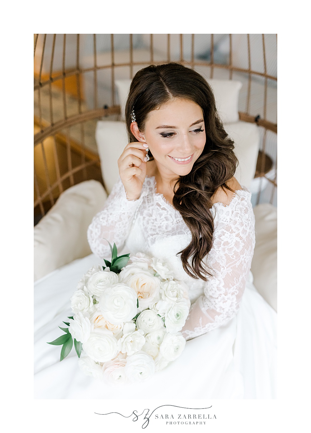 bride adjusts earrings inside egg chair with ivory and pale pink bouquet 