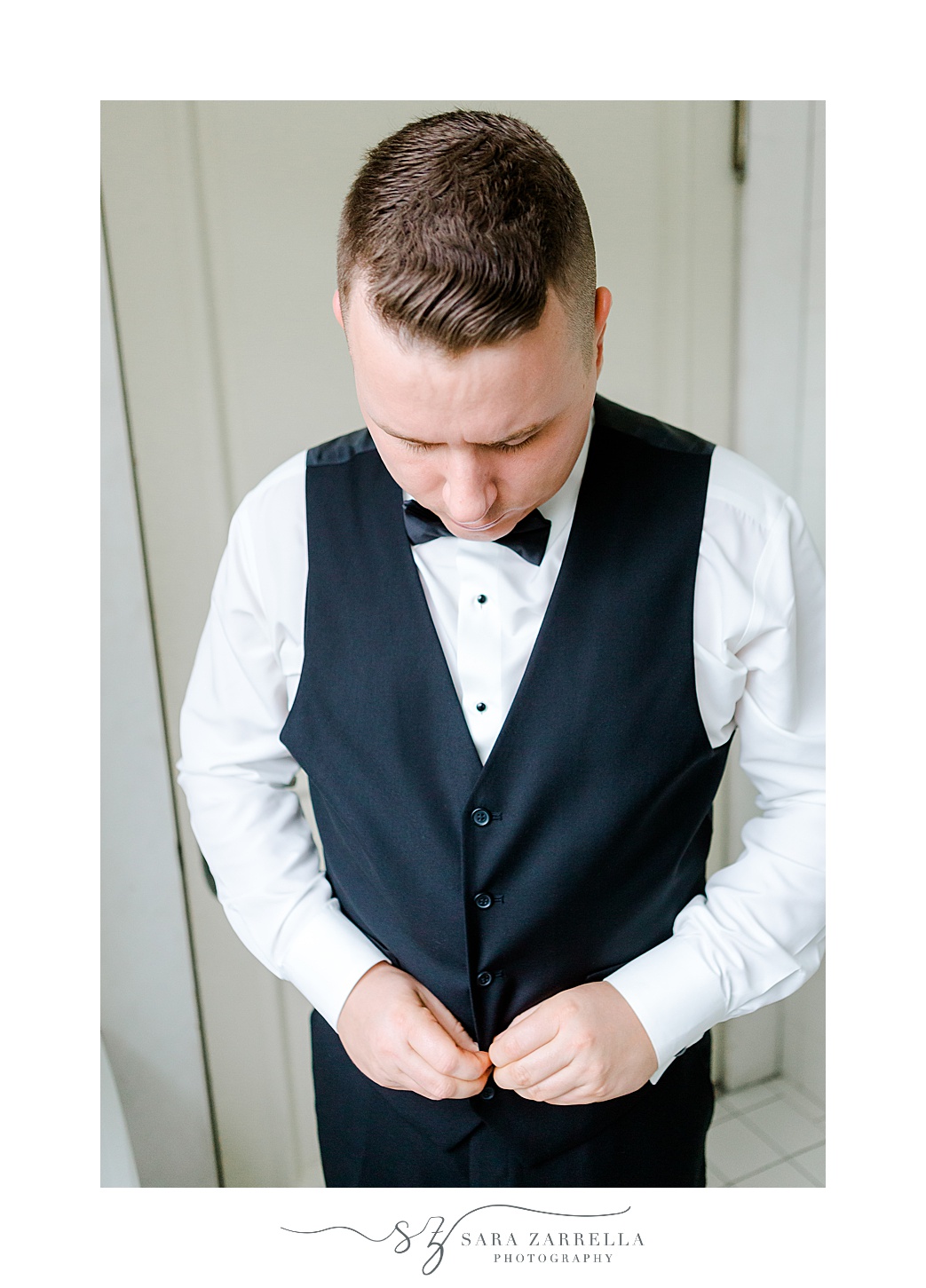 groom buttons up navy vest before RI wedding day