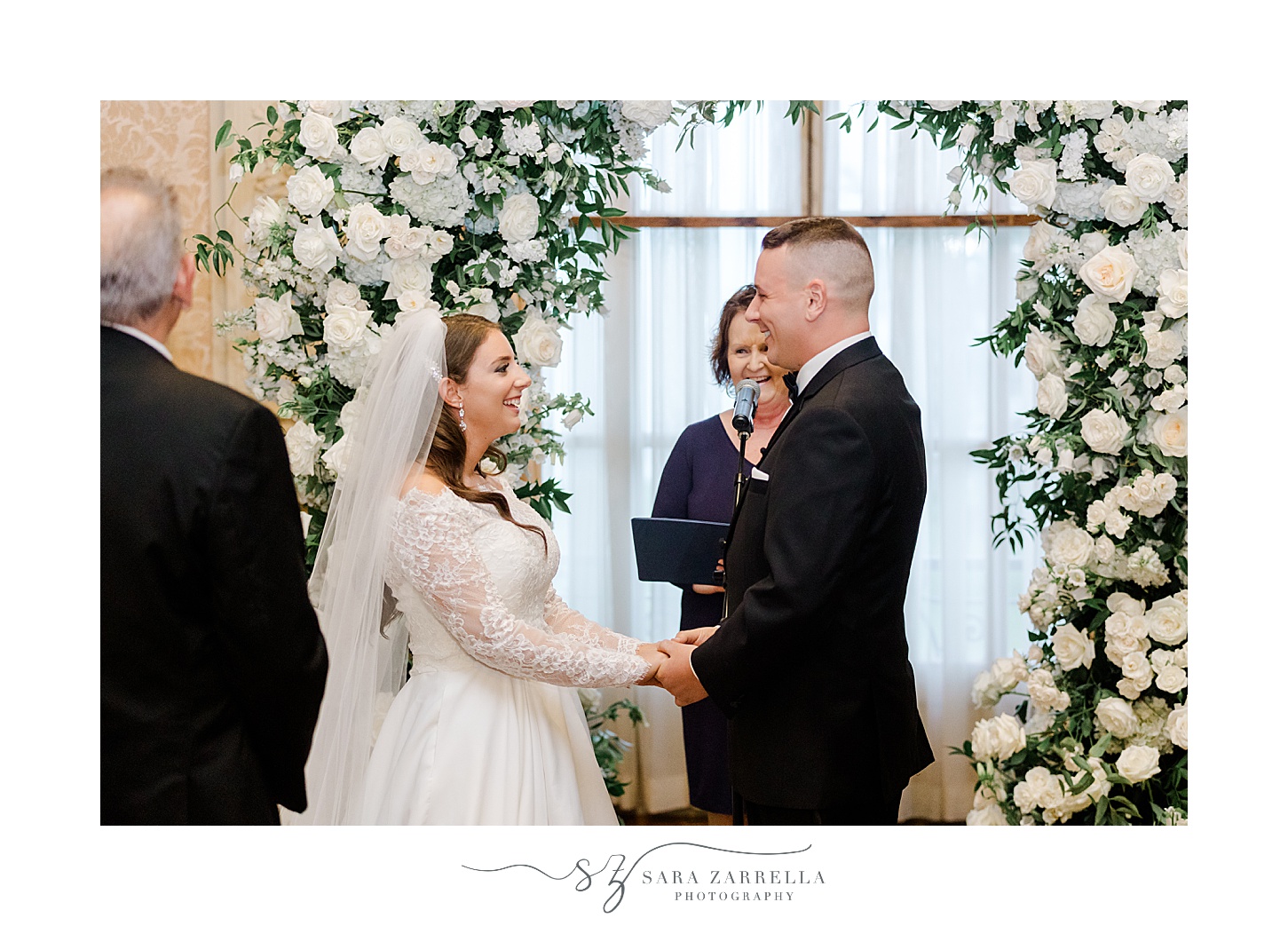  newlyweds stand in front of floral arbor inside wedding ceremony at Rosecliff Mansion
