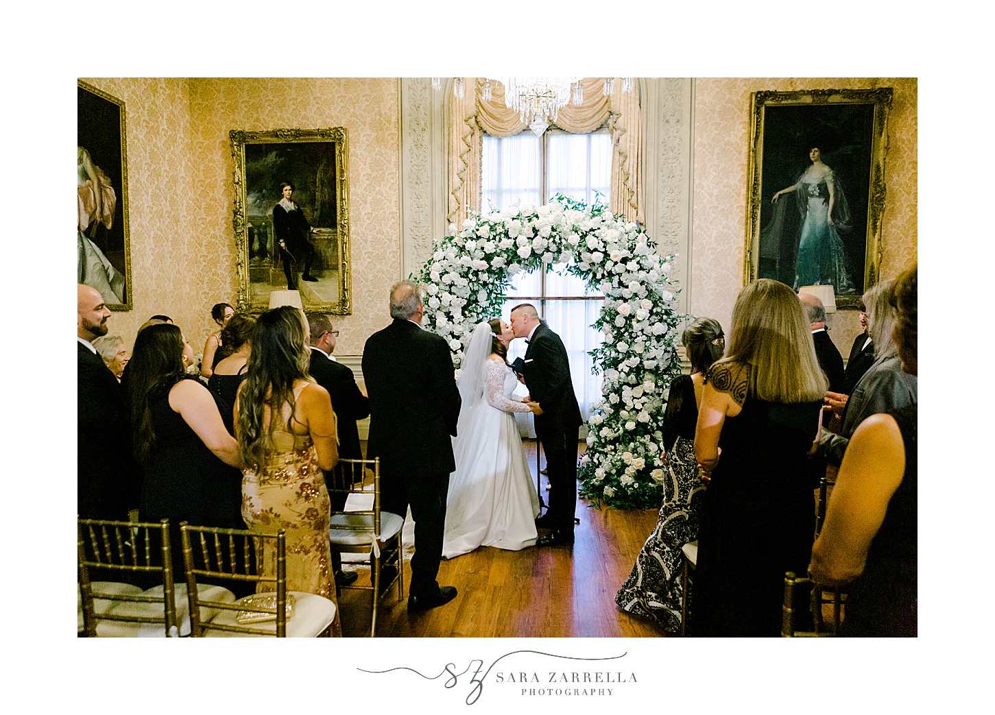 newlyweds kiss under white and green floral arbor inside wedding ceremony at Rosecliff Mansion