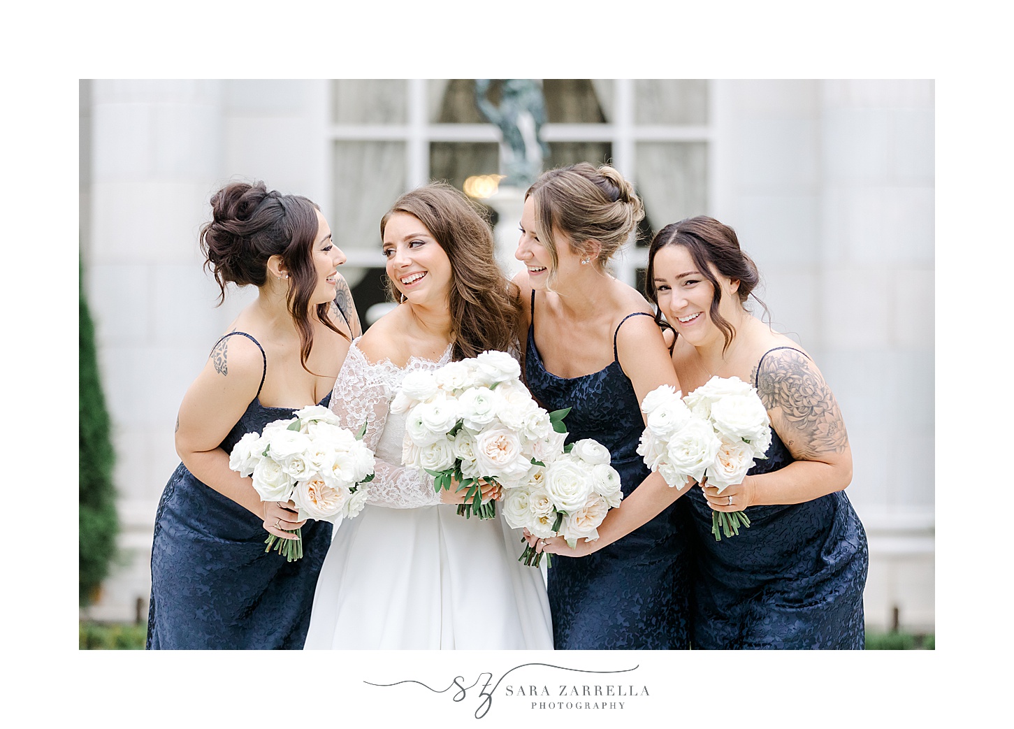 bride laughs with bridesmaids in navy gowns outside Rosecliff Mansion