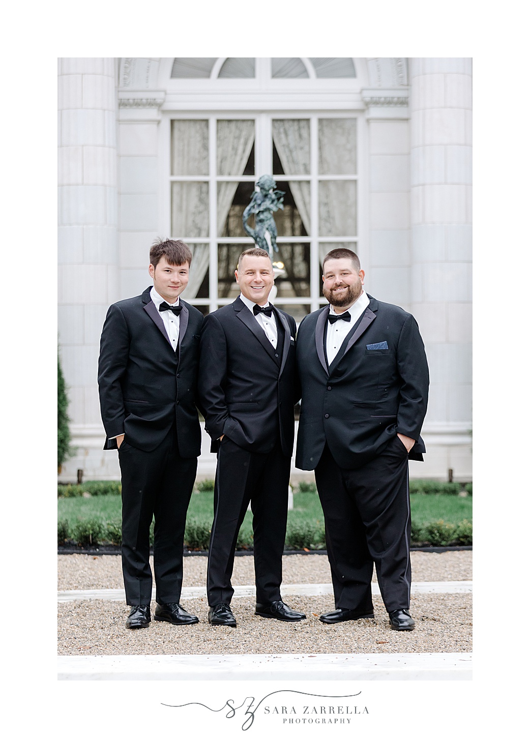 groom stands with groomsmen in black suits outside Rosecliff Mansion