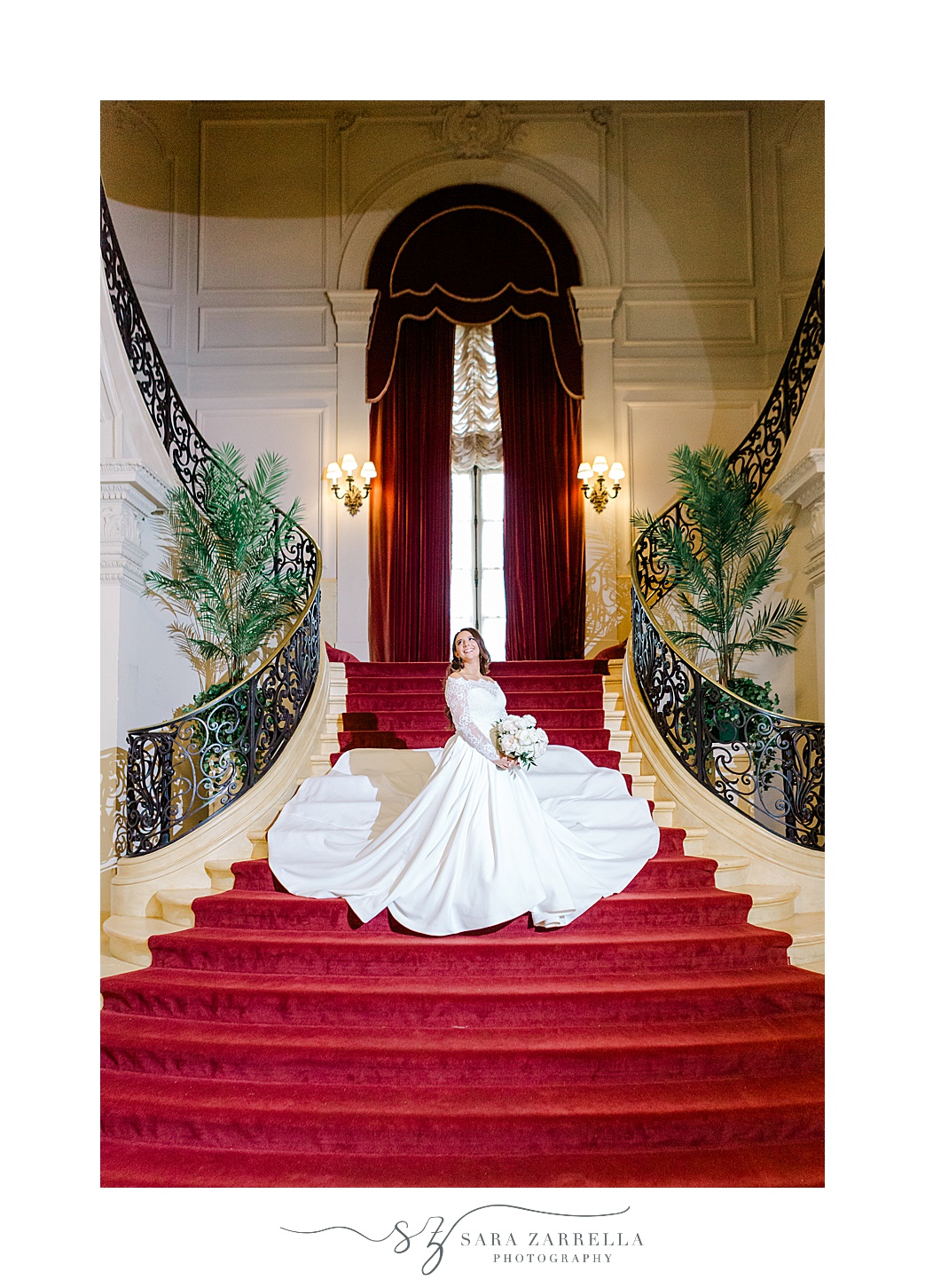 bride stands on staircase with red carpeting inside Rosecliff Mansion