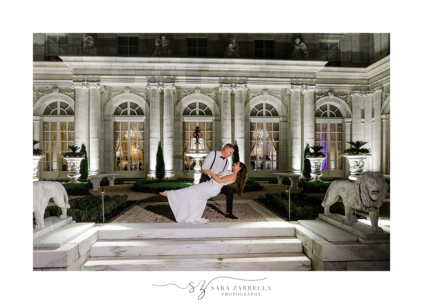 groom dips bride during nighttime portraits outside Rosecliff Mansion