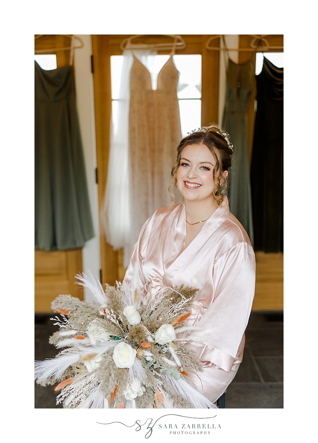 bride sits in front of green bridesmaid gowns holding big boho bouquet with feathers