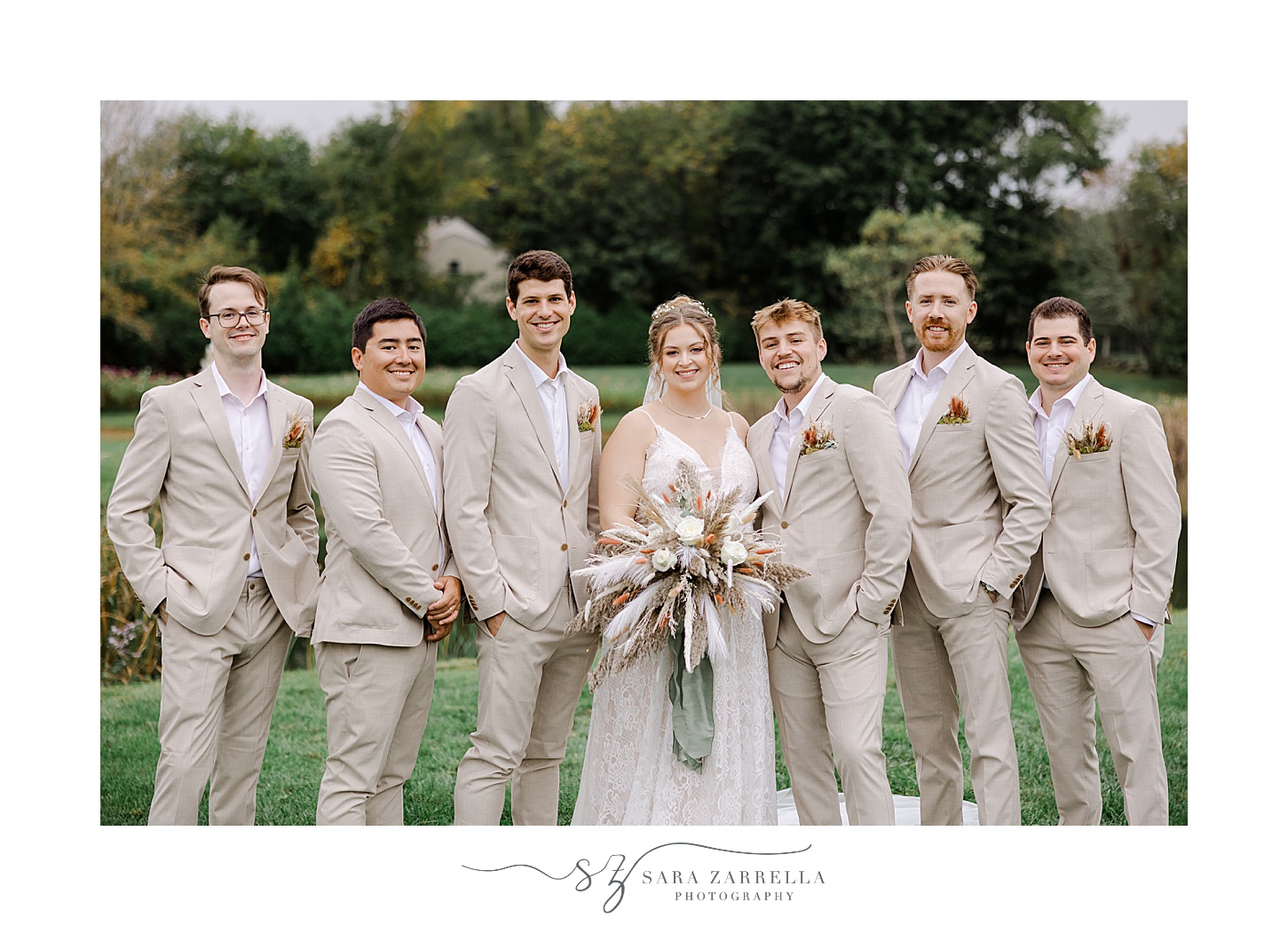 groomsmen in tan linen suits pose with bride on lawn in Rhode Island
