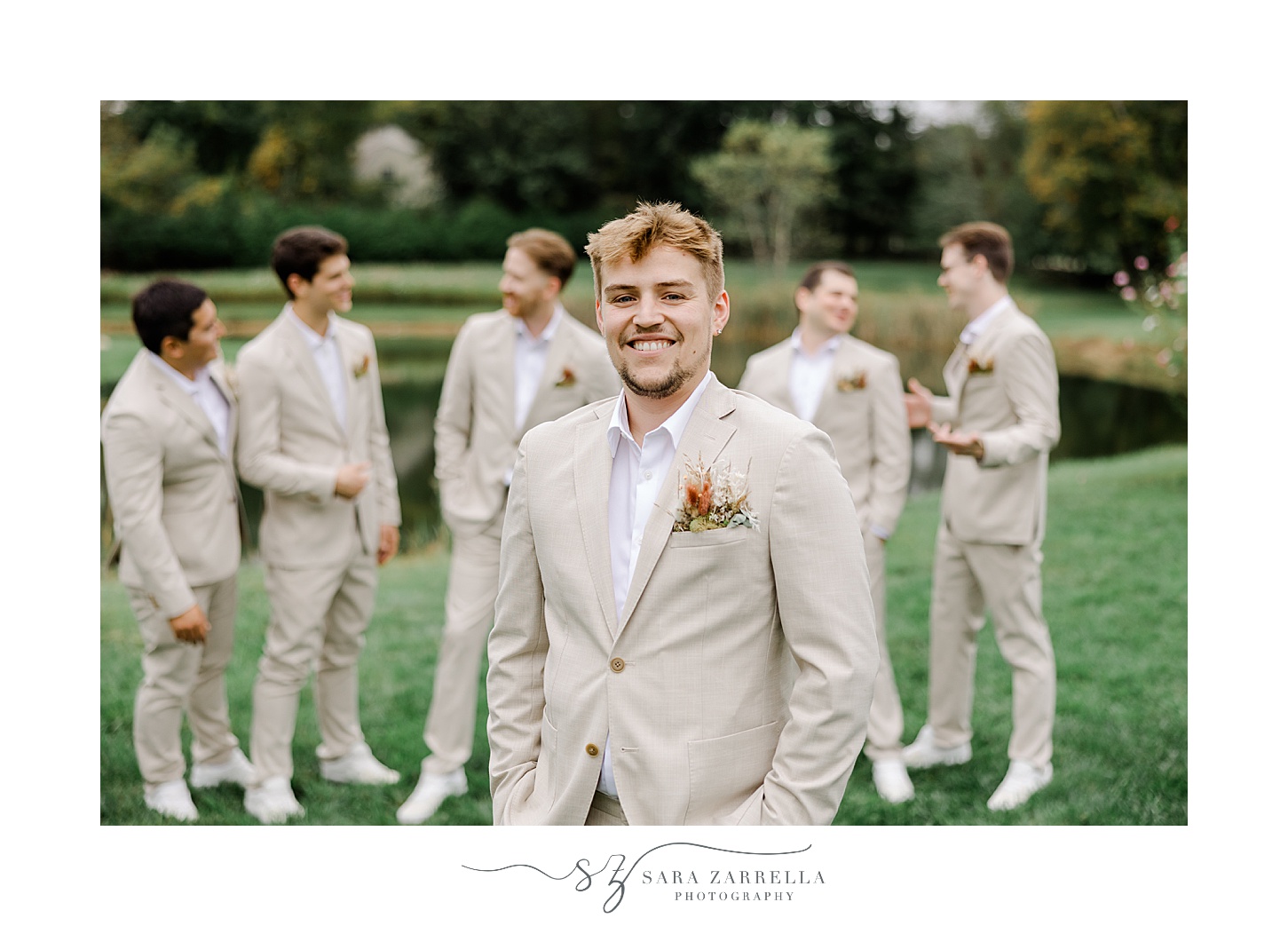 groom stands with groomsmen in tan suits on green lawn in Rhode Island