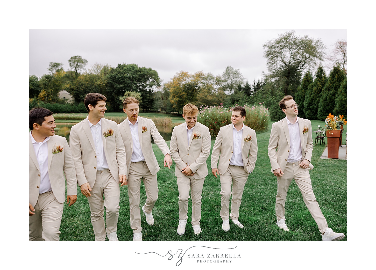groom stands with groomsmen in tan suits on green lawn in Rhode Island