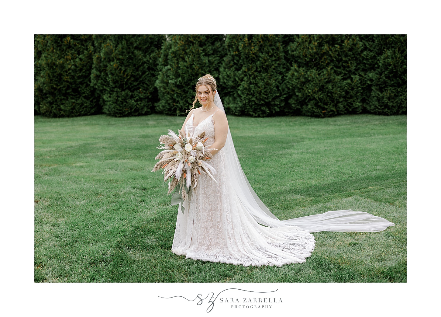 bride holds bouquet of boho flowers and feathers on lawn in Rhode Island