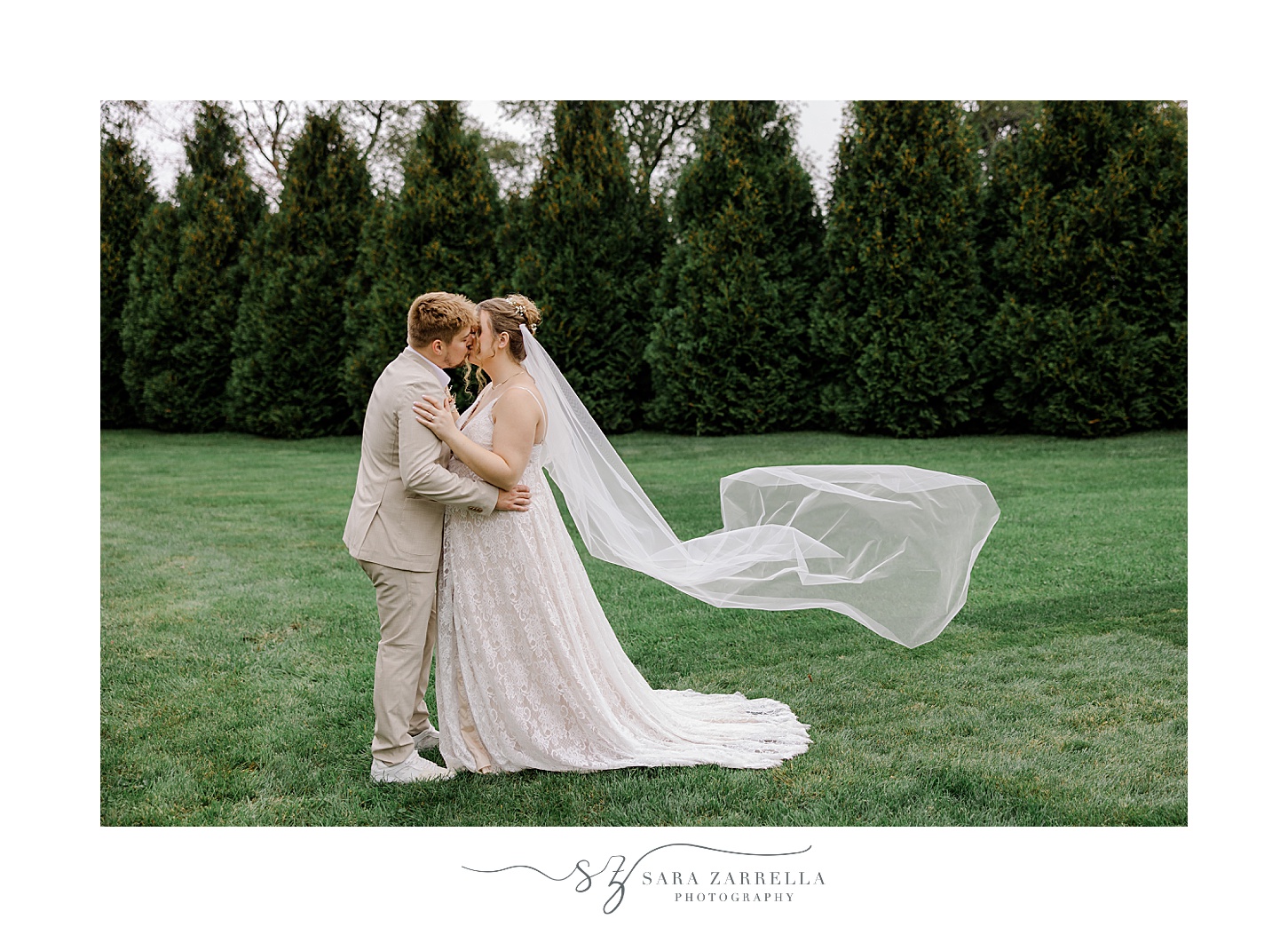 newlyweds kiss on lawn with bride's veil floating behind them on Rhode Island wedding day