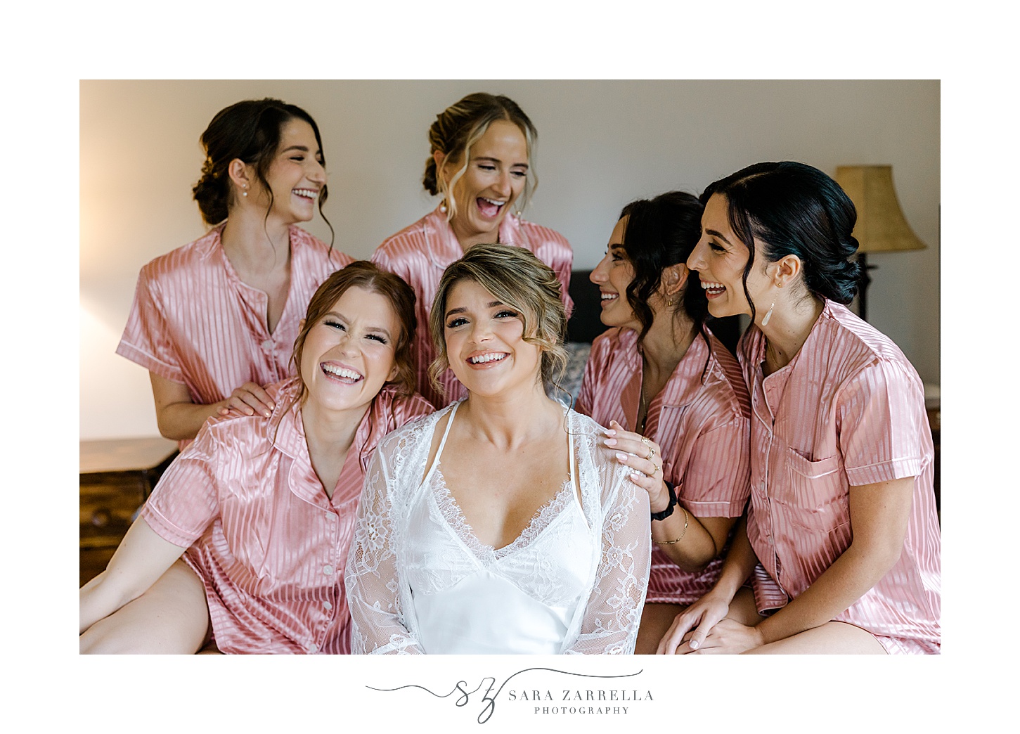 bride sits with bridesmaids in pink robes on bed in Rhode Island 