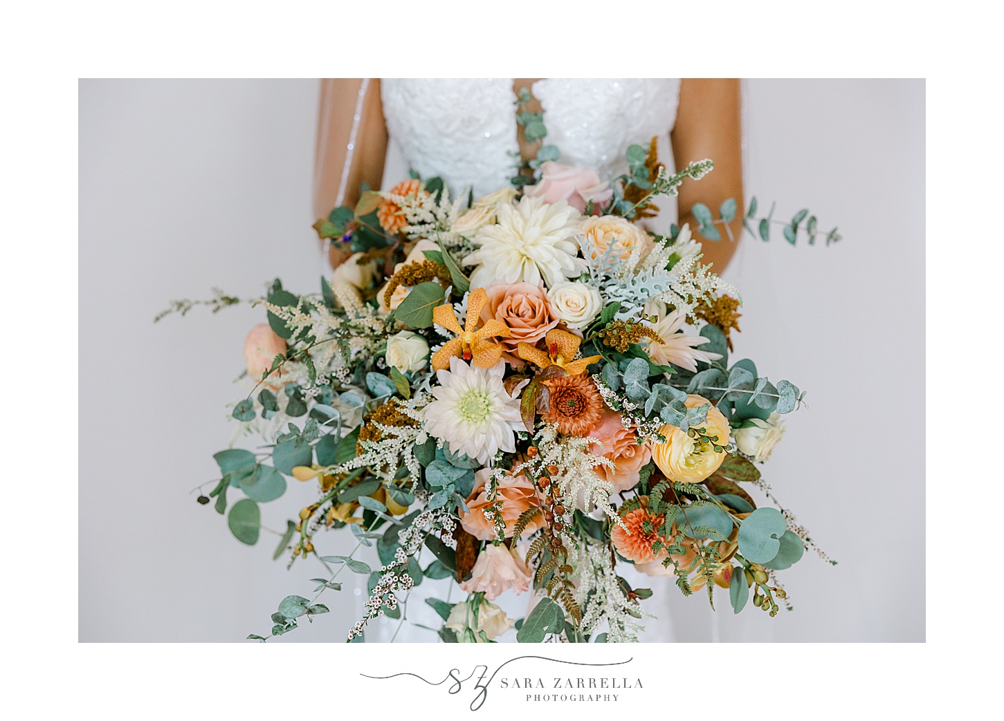 bride holds bouquet of orange and yellow flowers with greenery 