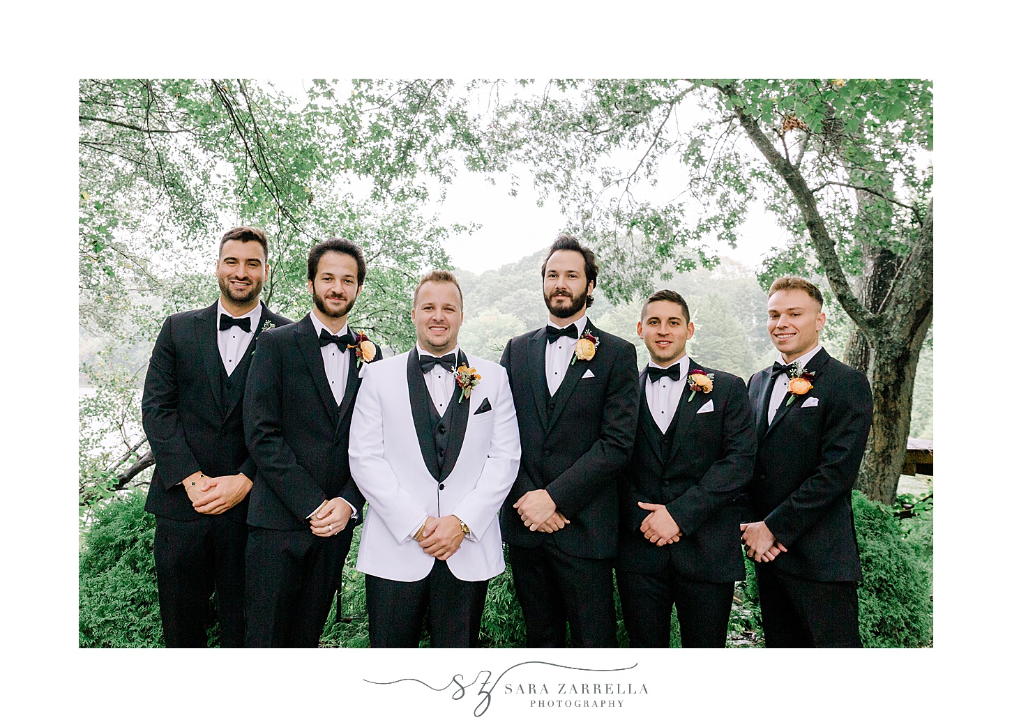 groom in white jacket with black lapel stands with groomsmen in black suits 