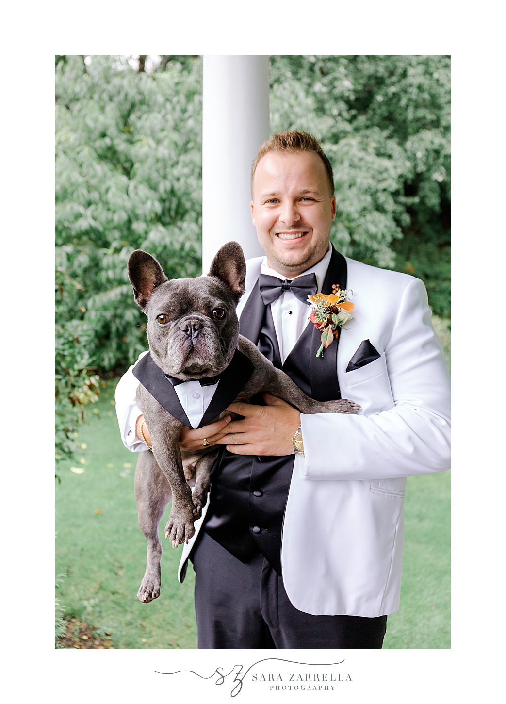 groom holds dog in white suit jacket with black lapel