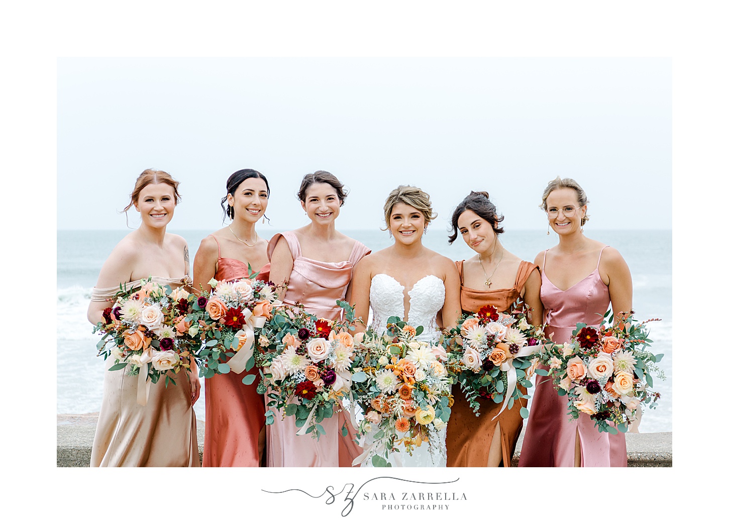 bride poses with bridesmaids in pink gowns in front of oceanfront in Westerly RI