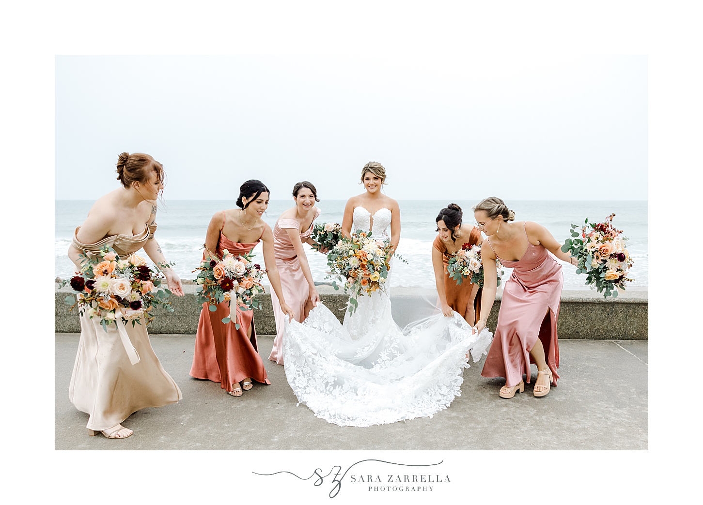 bridesmaids help bride with skirt of wedding gown in front of oceanfront in Westerly RI