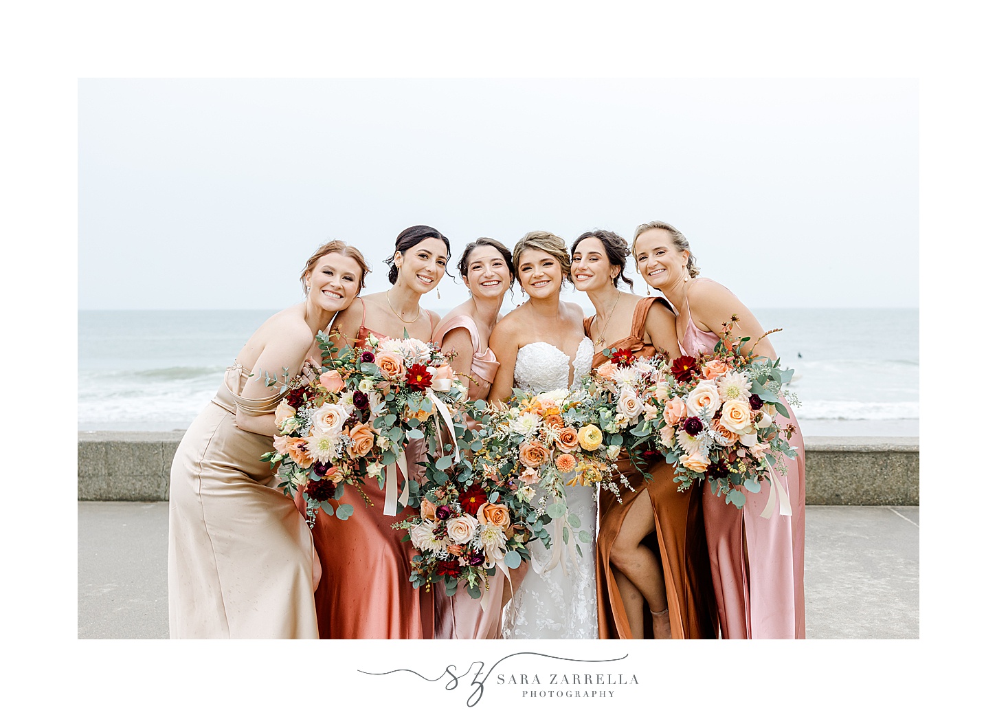 bride and bridesmaids hug close together in front of waterfront in Rhode Island 