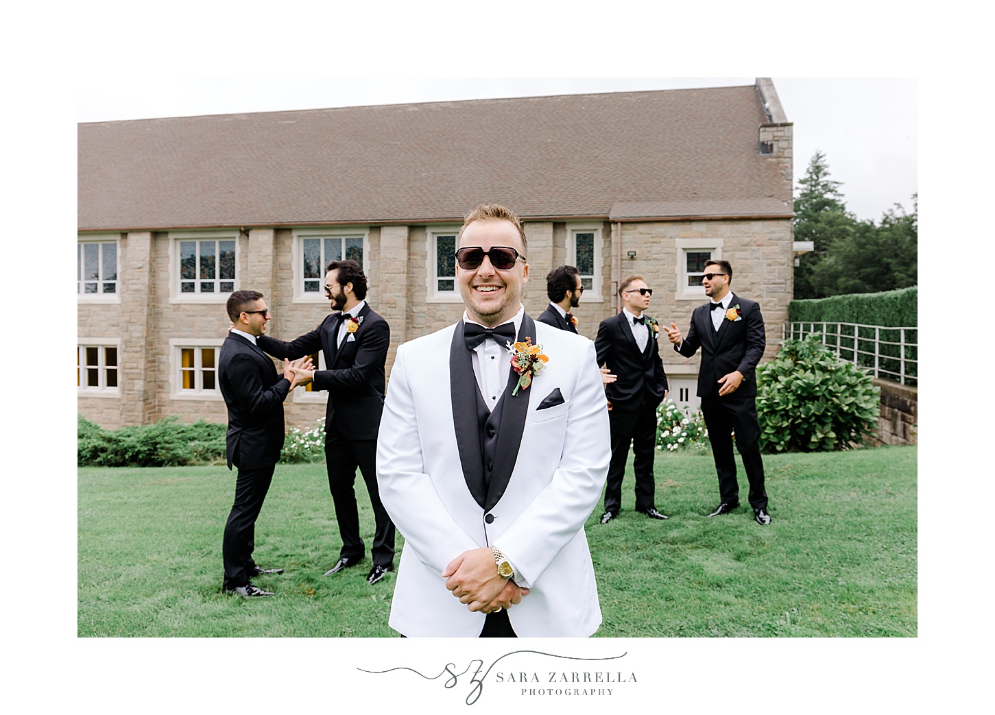 groom in white suit jacket with black lapel poses in front of St Pius Church