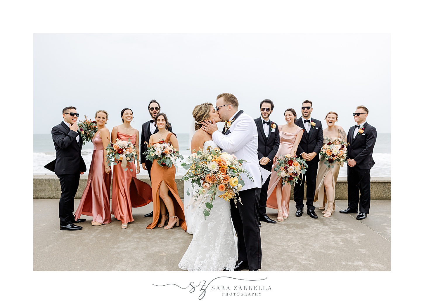 newlyweds kiss with bridal party in front of ocean in Westerly RI