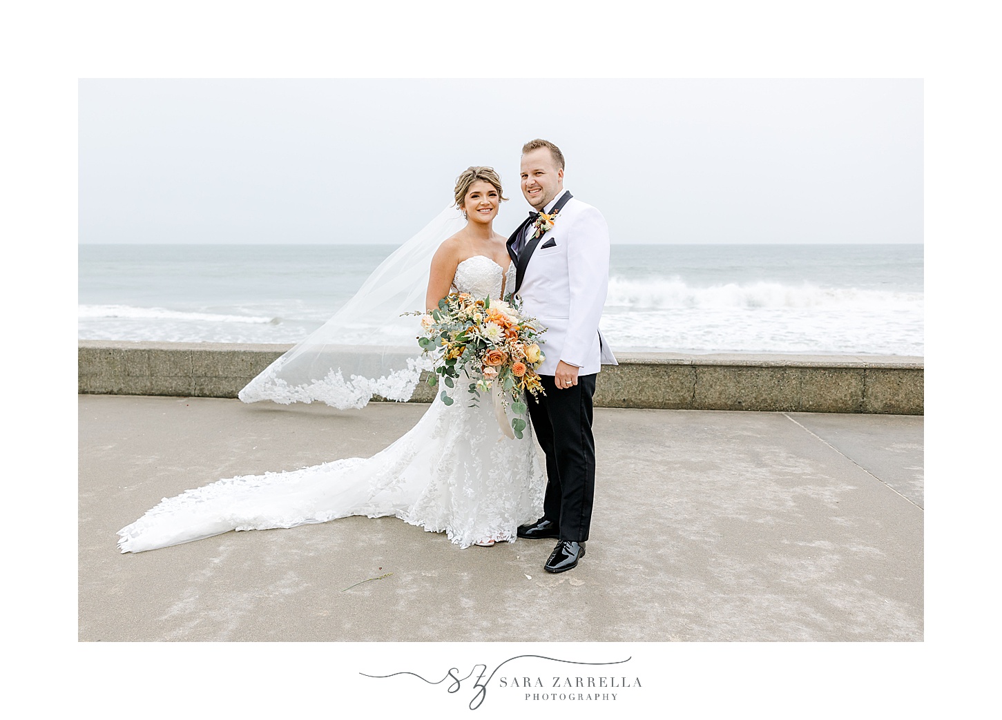 newlyweds hug with bride's veil floating behind them at beachfront in Westerly RI