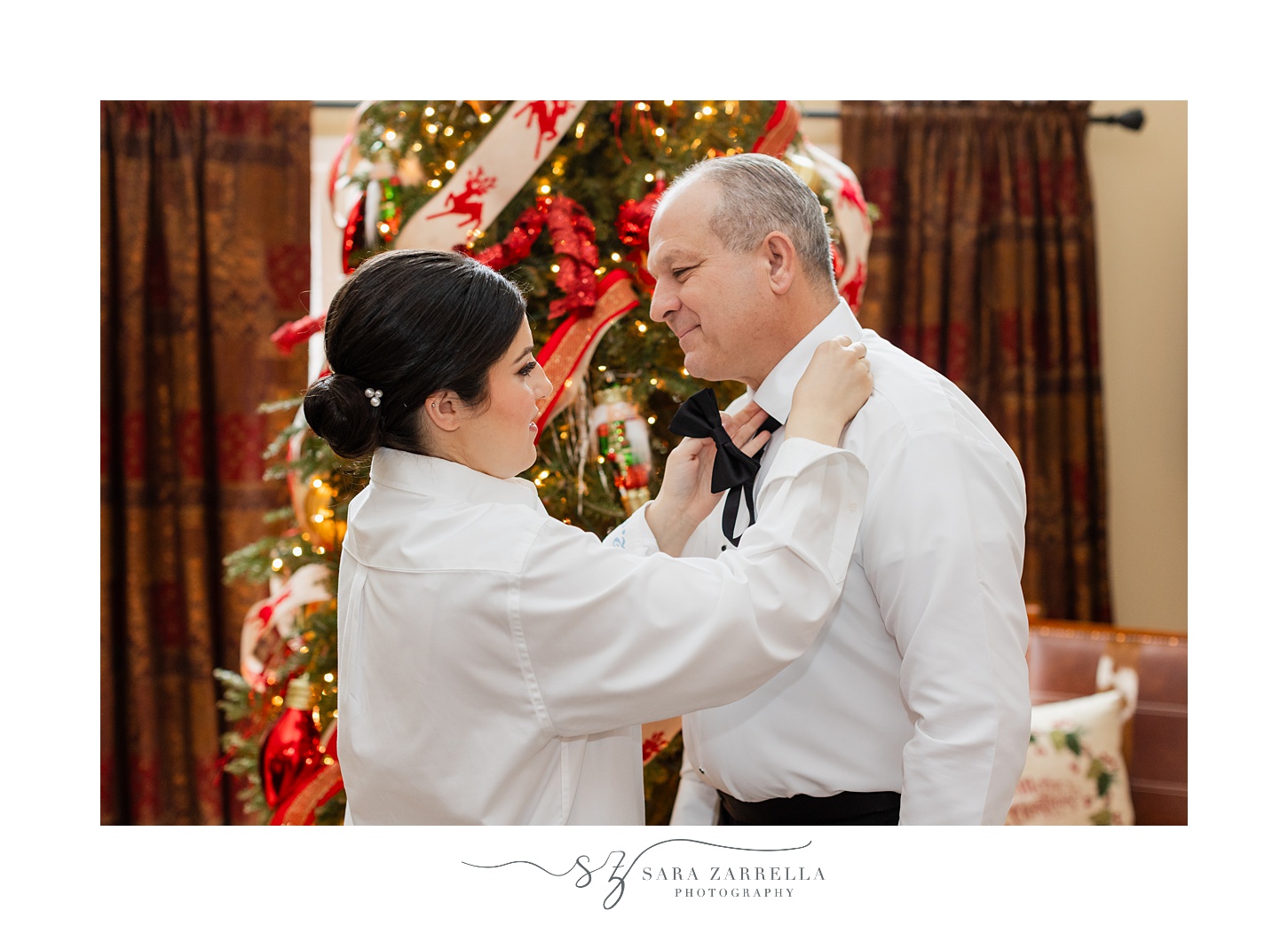 bride helps father with tie in front of Christmas tree 