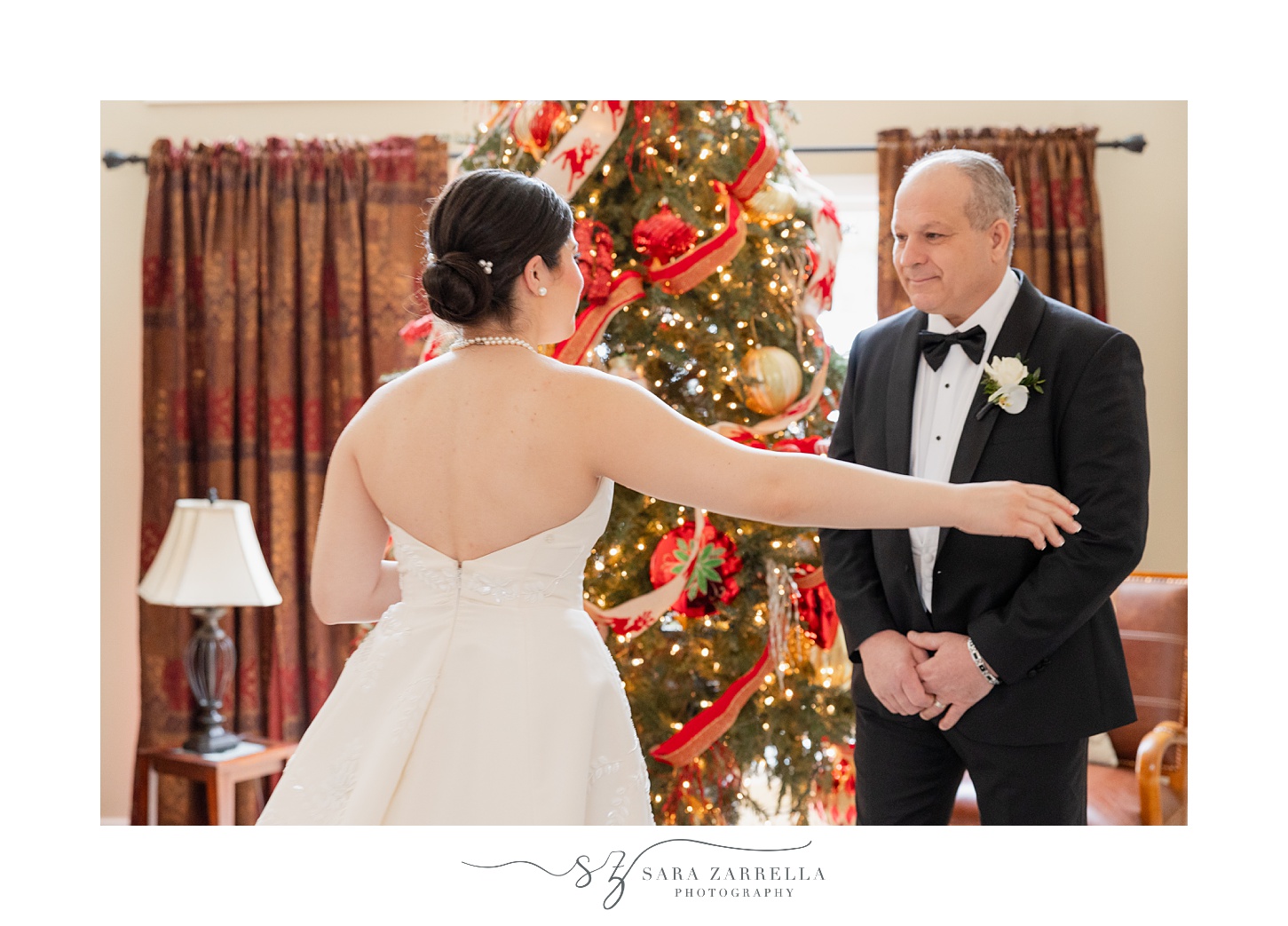 bride reaches for father during first look by Christmas tree