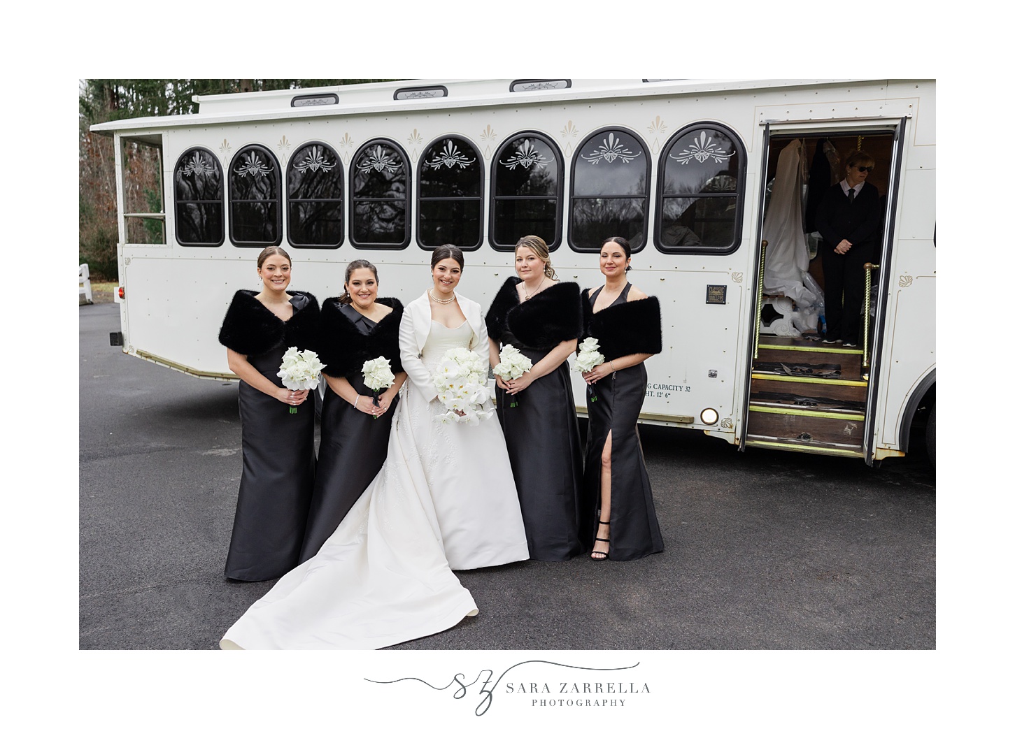 bride stands with bridesmaids in black dresses outside white trolley 