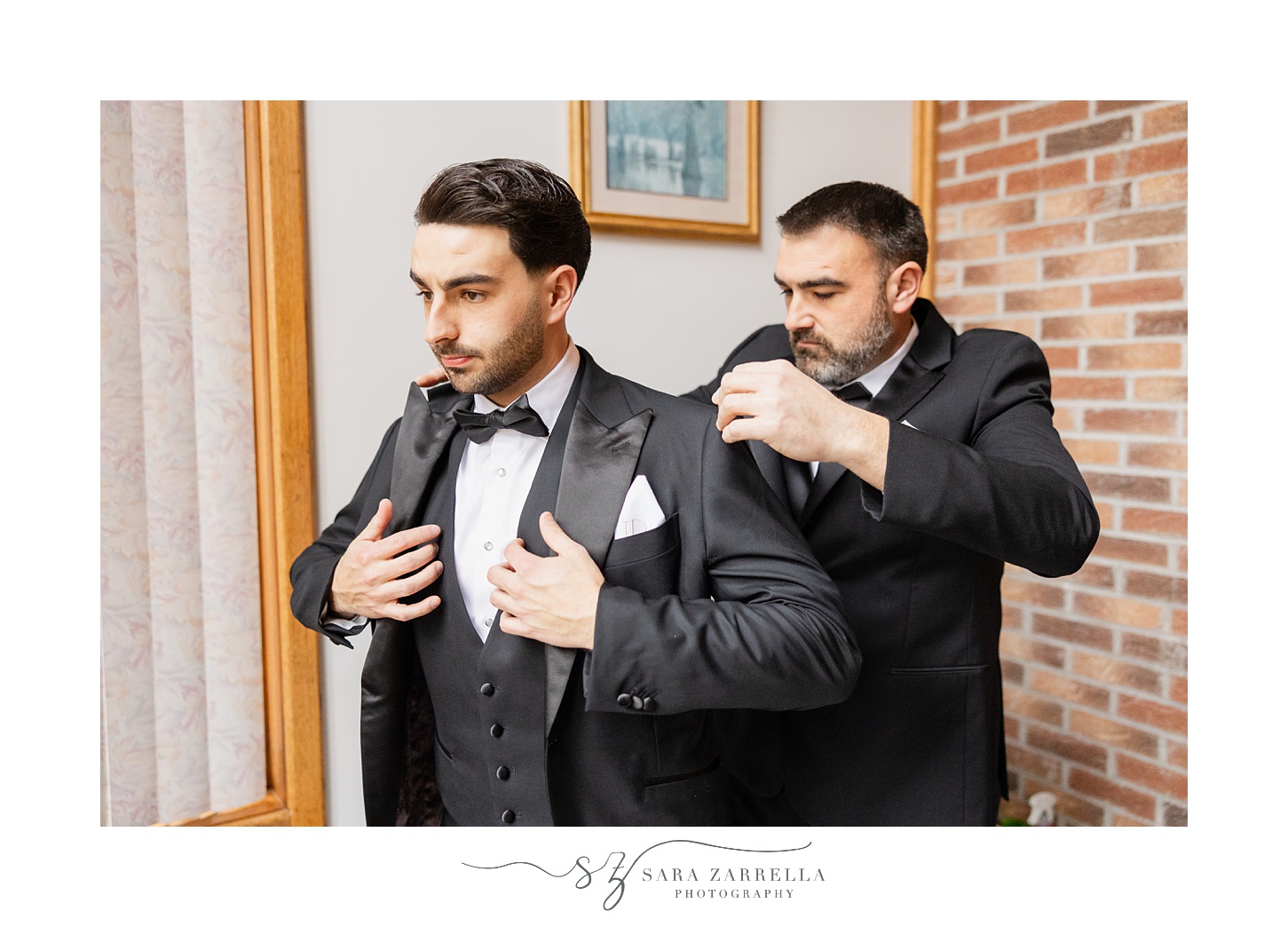 groomsman helps groom into black suit jacket 