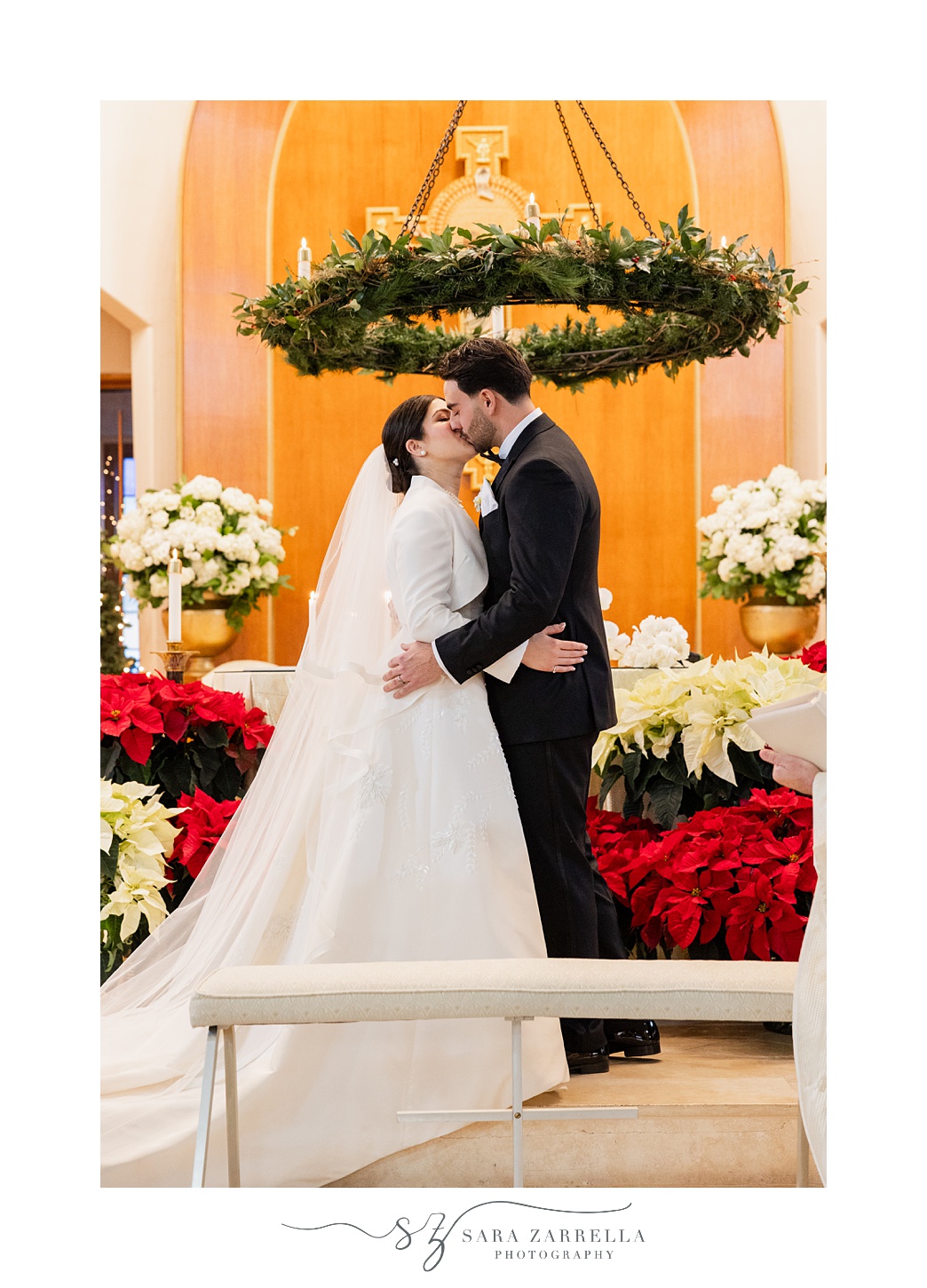 newlyweds kiss under hanging greenery lined chandelier inside St. Thomas Church in Providence RI