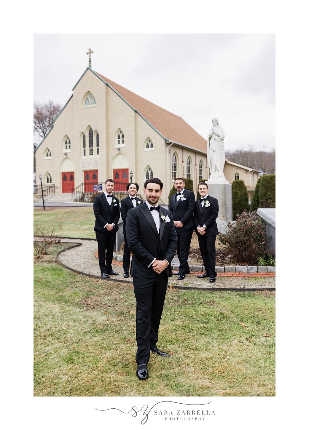 groom stands outside church in Providence RI with groomsmen behind him